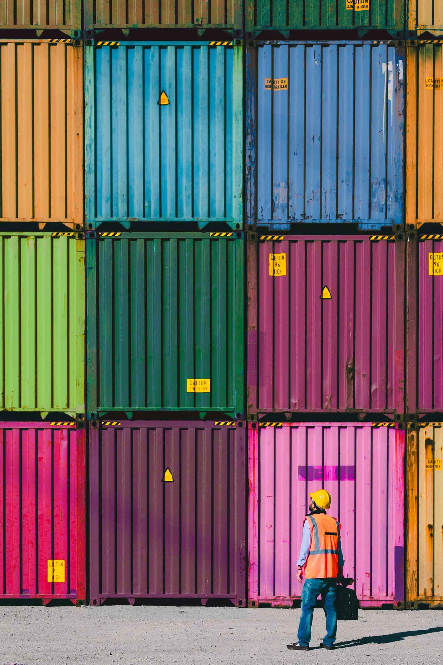 A man is walking in front of a stack of colorful shipping containers.