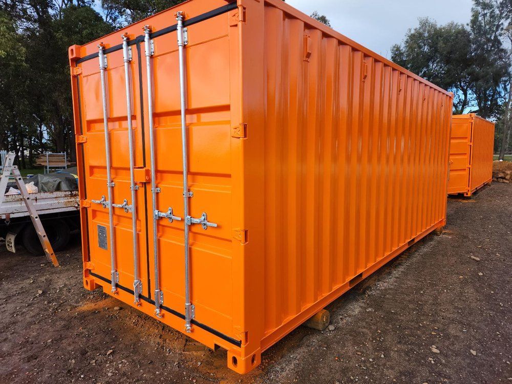 A row of orange shipping containers are parked in a dirt lot.