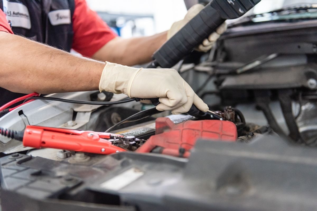 Mechanic using jumper cables to jump-start a car battery in an engine bay.