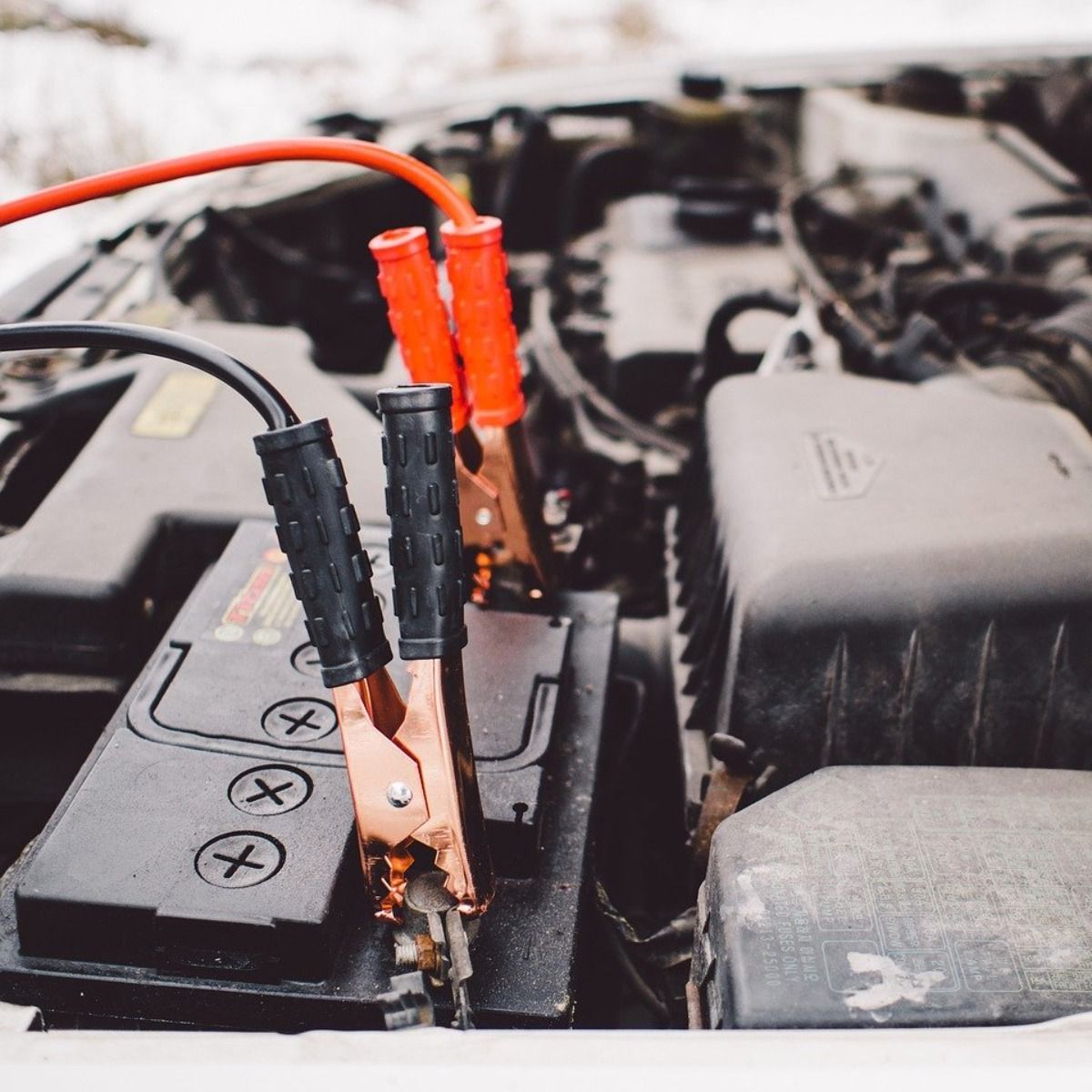 Jumper cables connected to a car battery, with red and black clamps, in an engine bay.