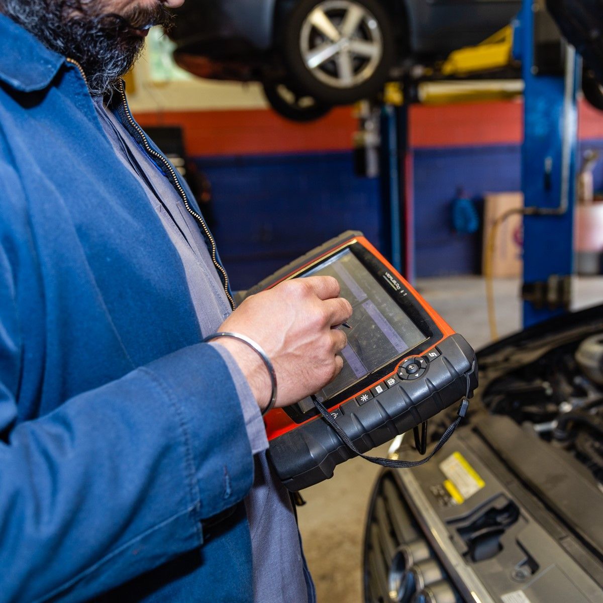 Mechanic using a diagnostic scanner on a car in a repair shop.