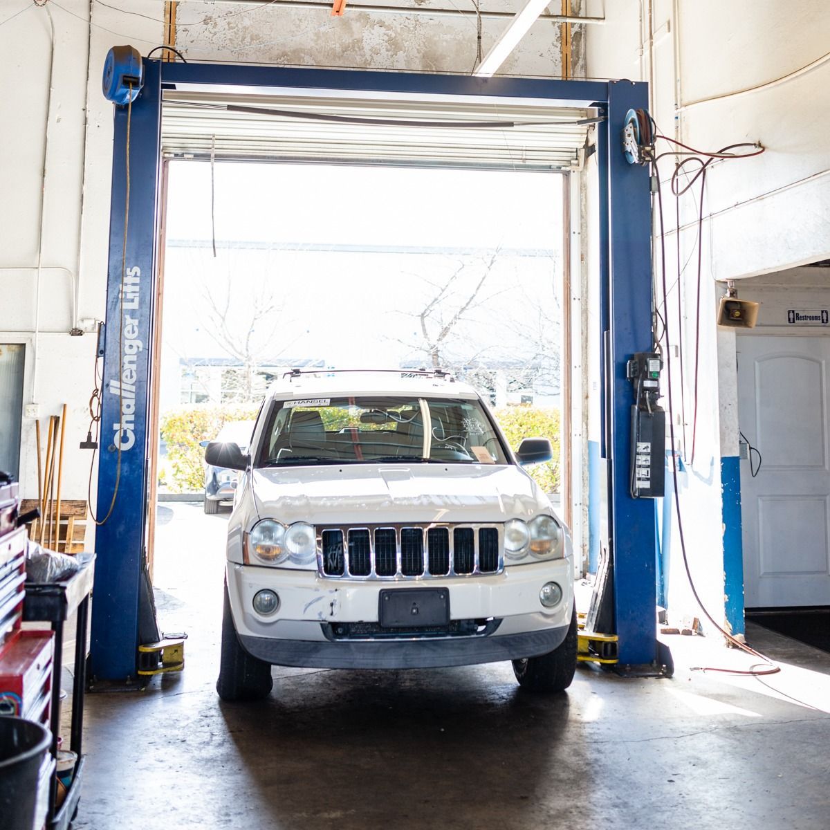 SUV on a lift in a garage. Blue lift, white SUV, open garage door, bright light.