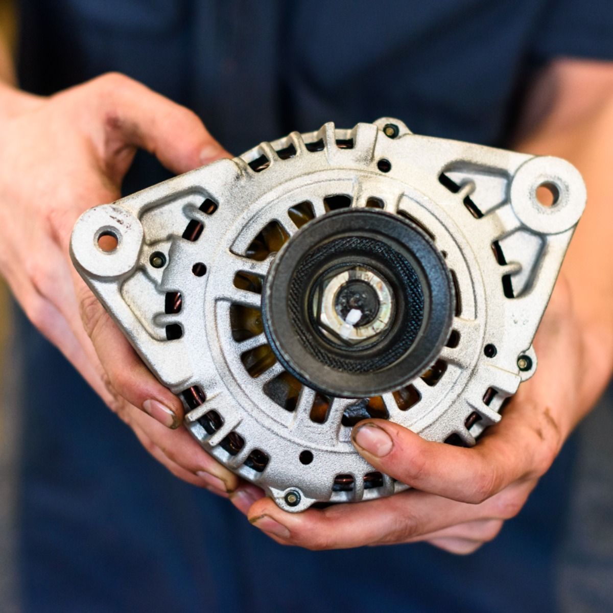 Hands holding a car alternator, a metallic, circular component.