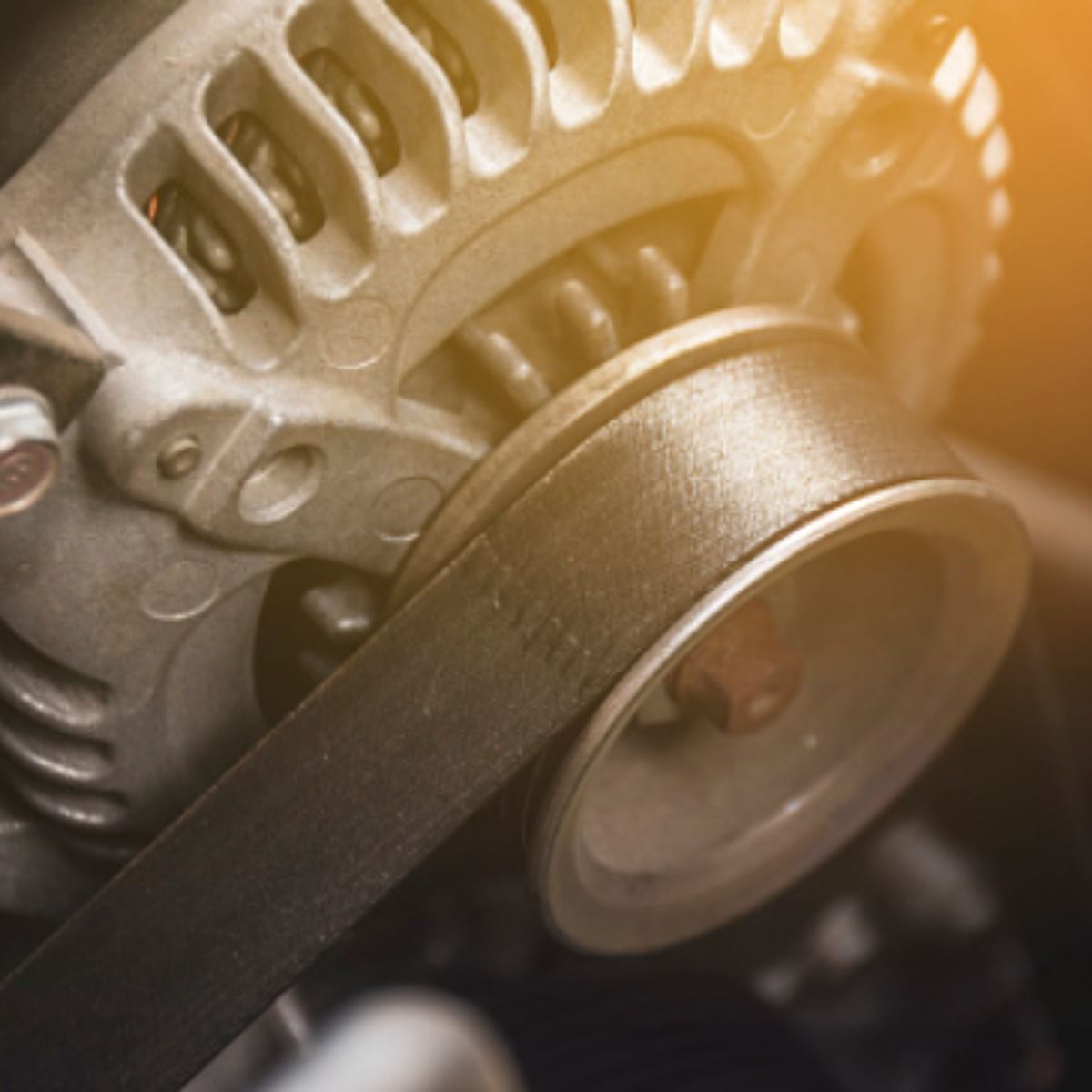 Close-up of a car alternator with a belt wrapped around the pulley.  The lighting is warm and bright.