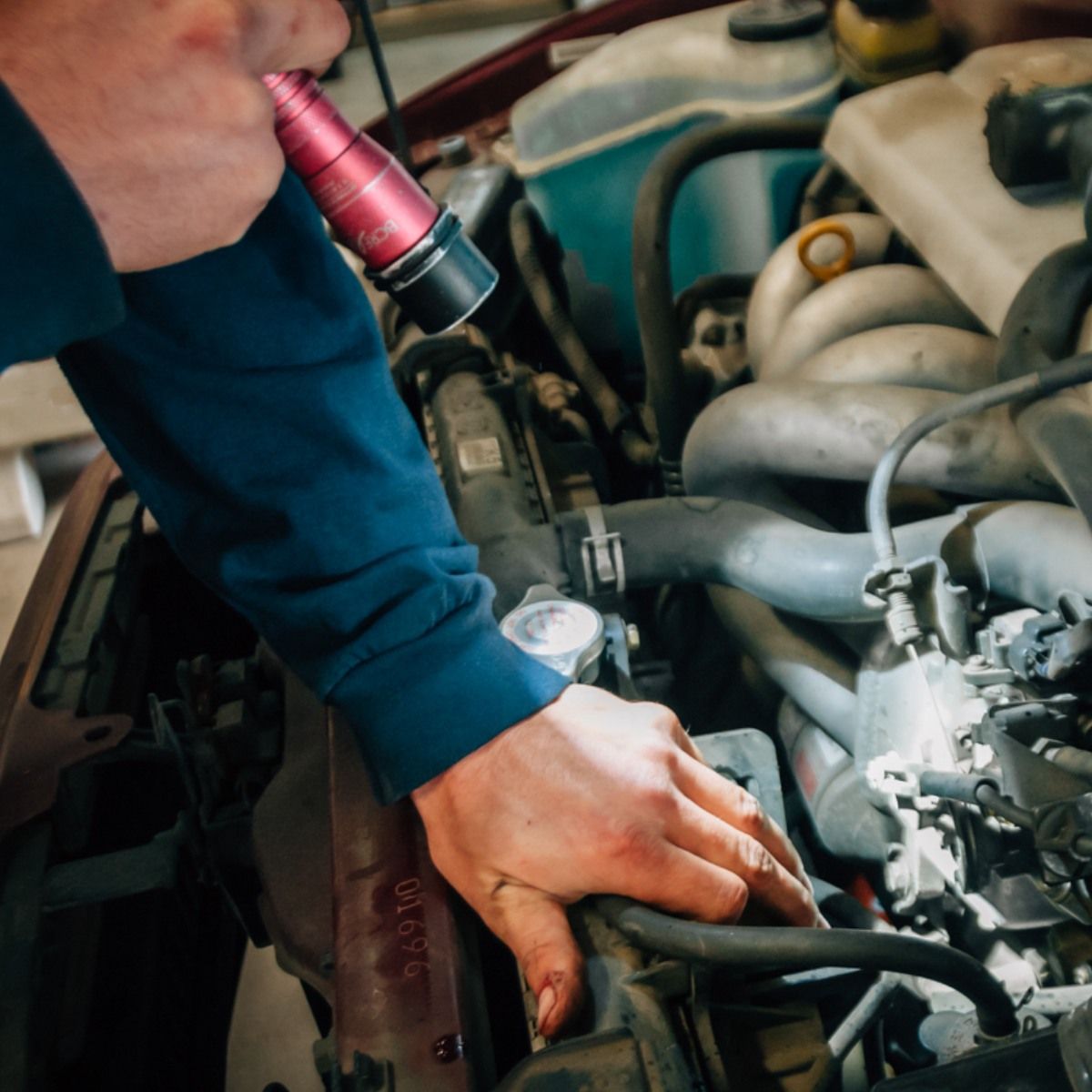Person in a dark blue shirt using a flashlight to inspect a car engine.