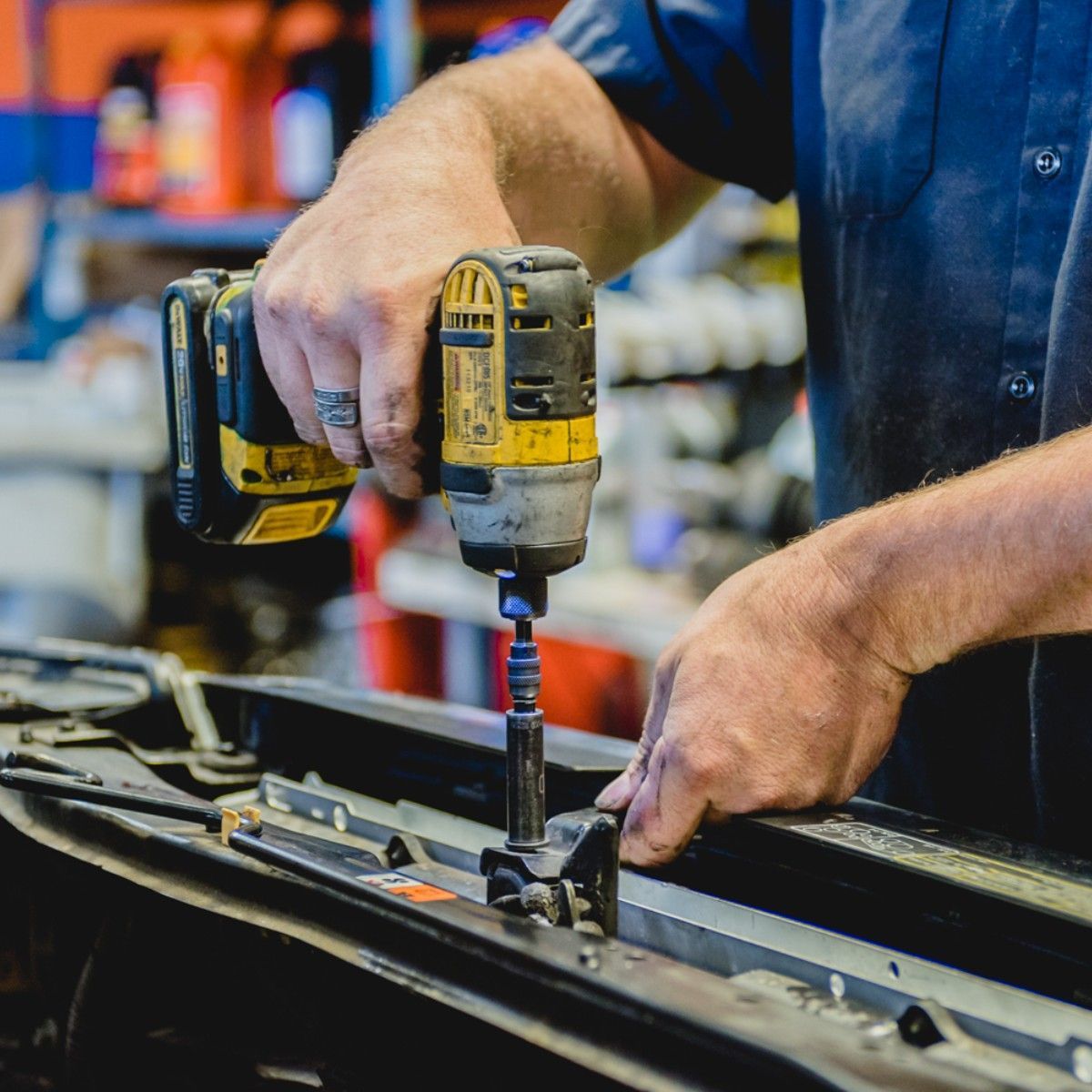 Mechanic using a yellow and black power drill to work on a car part.