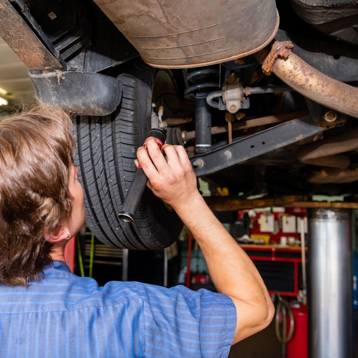 Mechanic working on a car from below, using a wrench. Garage setting, blue shirt.