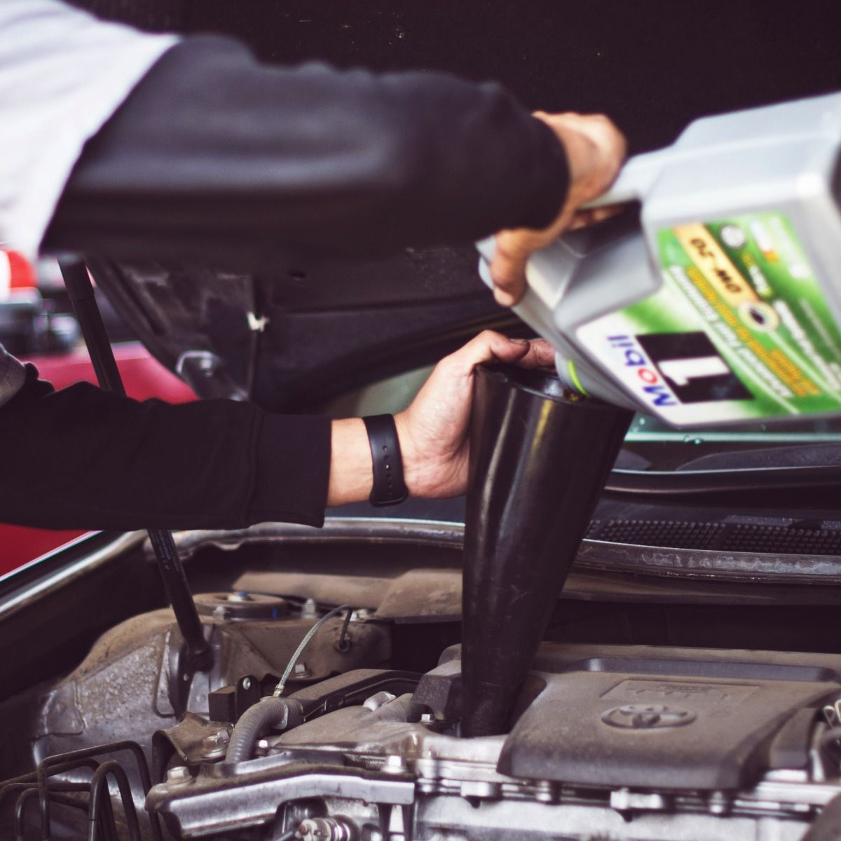 Person pouring motor oil into a car engine using a funnel.