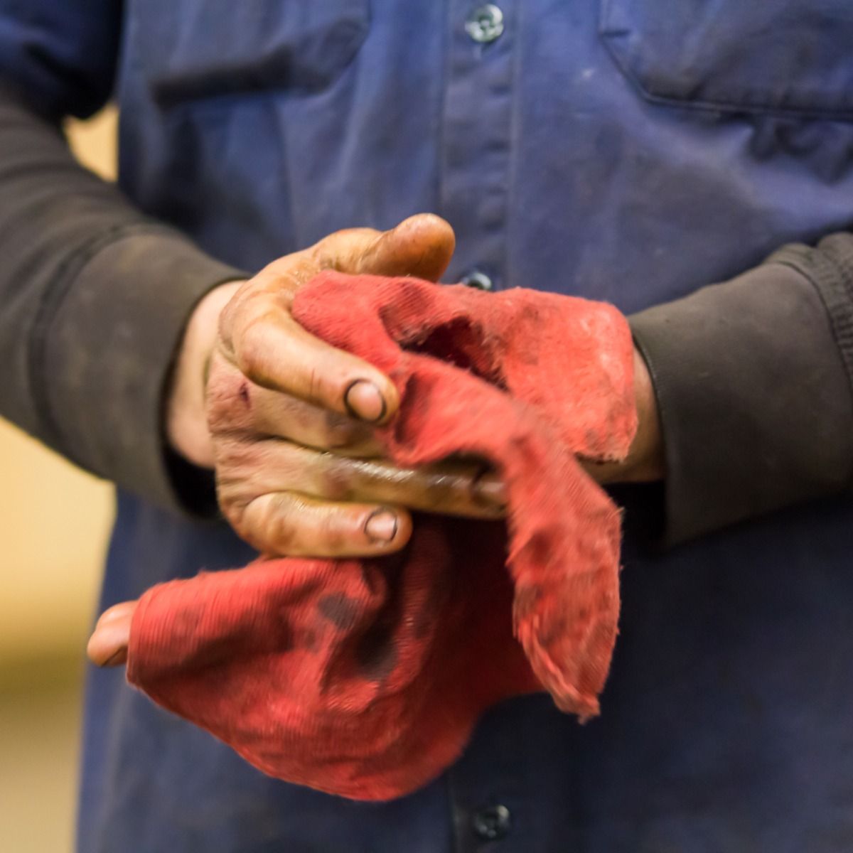 Hands covered in grease, holding a red rag; person in blue work shirt.