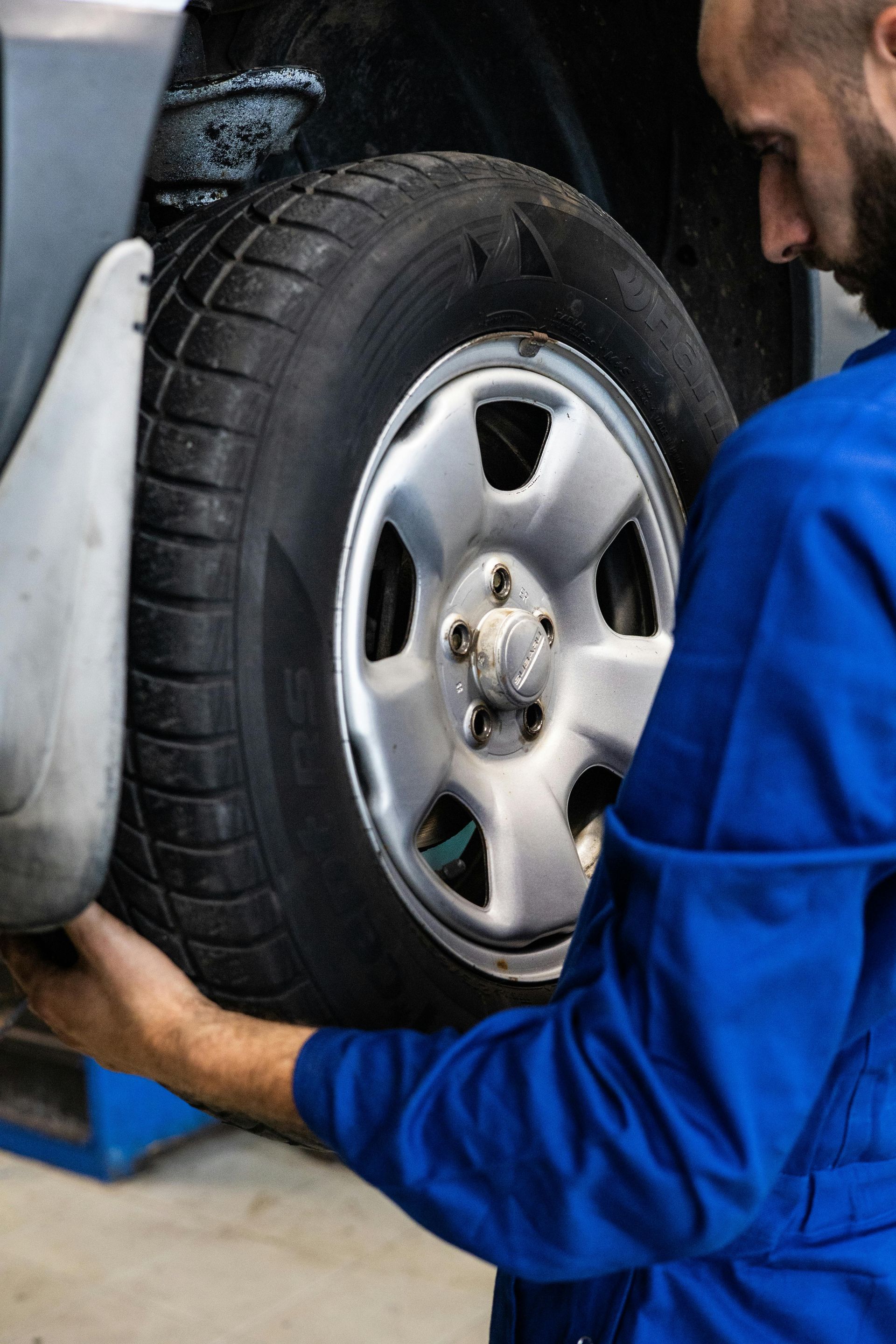 Mechanic in blue coveralls changing a car tire.