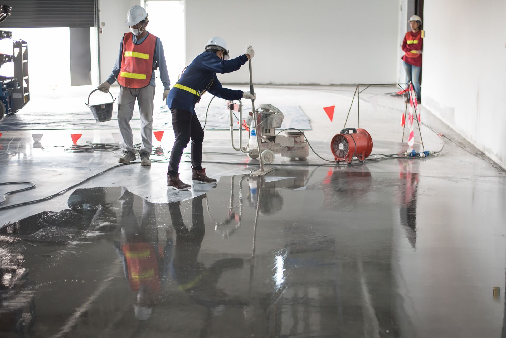 Workers in safety vests and helmets operate industrial floor polishing equipment on a wet, reflective indoor floor. — On The Grind In Moreton Bay, QLD