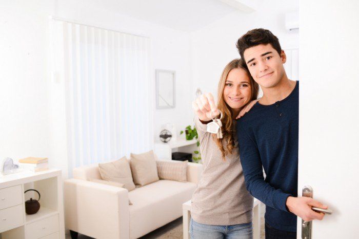 happy young couple welcoming in their new house showing the door keys at entrance door