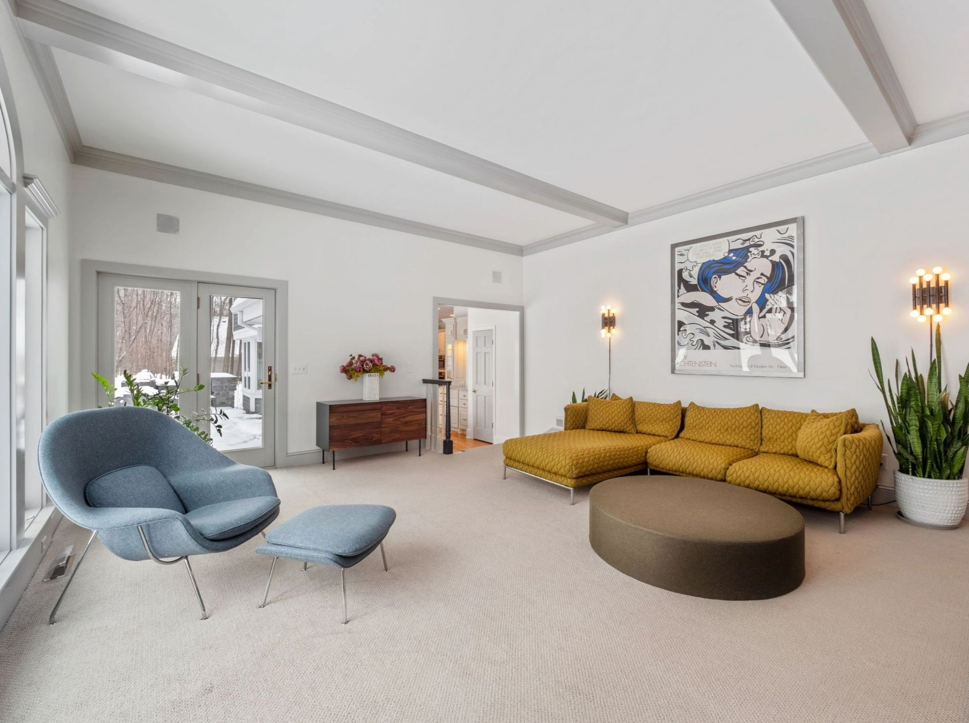 Living room with mustard-yellow sectional, blue chair, and large abstract art. Gray trim and white walls.