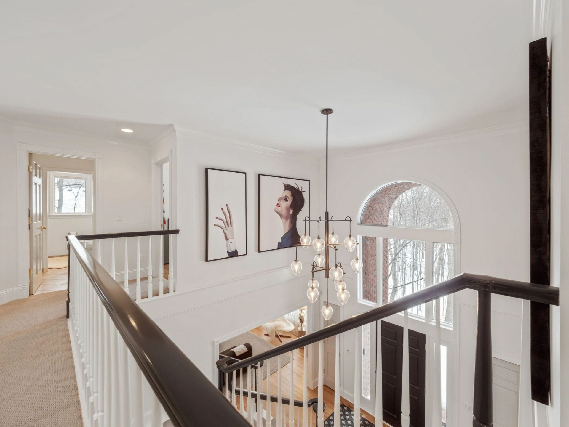 Hallway with staircase, white walls, black railing, modern chandelier, and two framed prints.