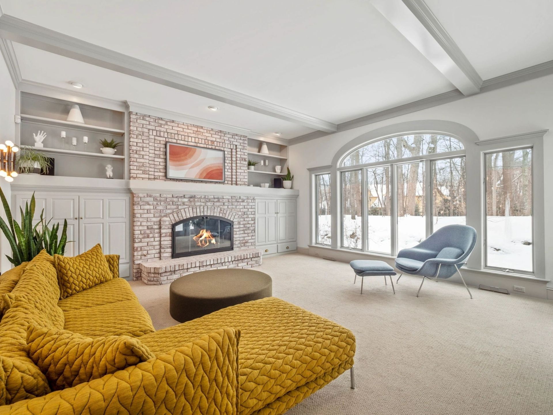 Living room with yellow couch, brick fireplace, and large windows looking out to a snowy landscape.