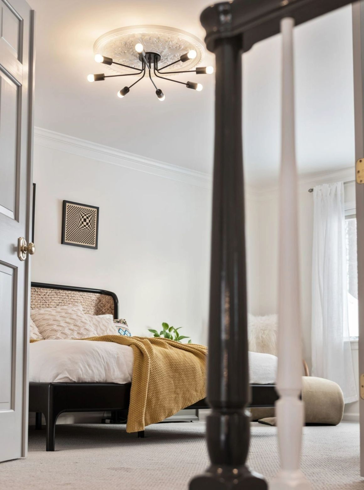 Bedroom interior with a black bed, ceiling light, and white walls. A black and white banister is in the foreground.