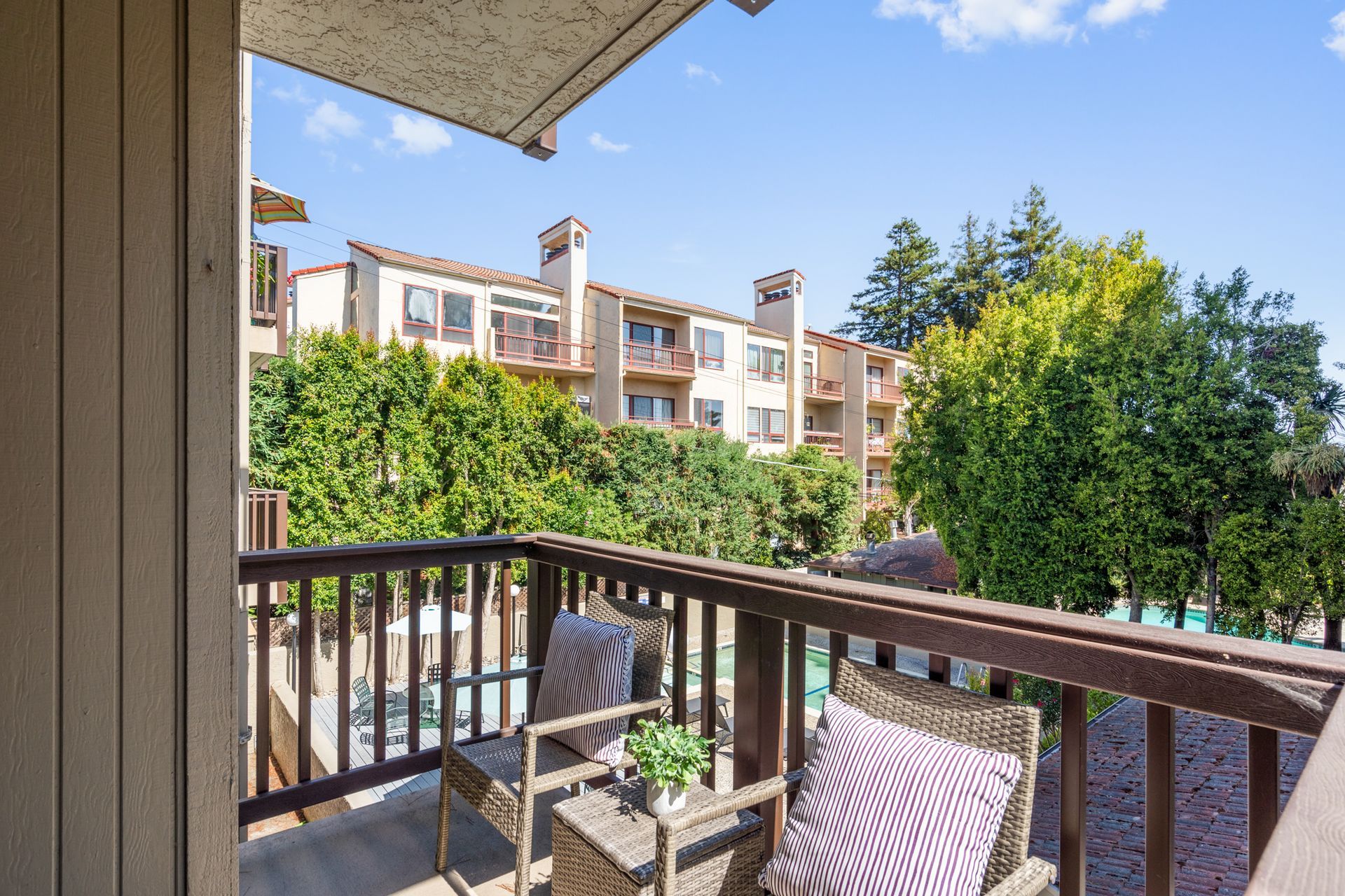 A balcony with a chair and a table with a view of a building and trees.