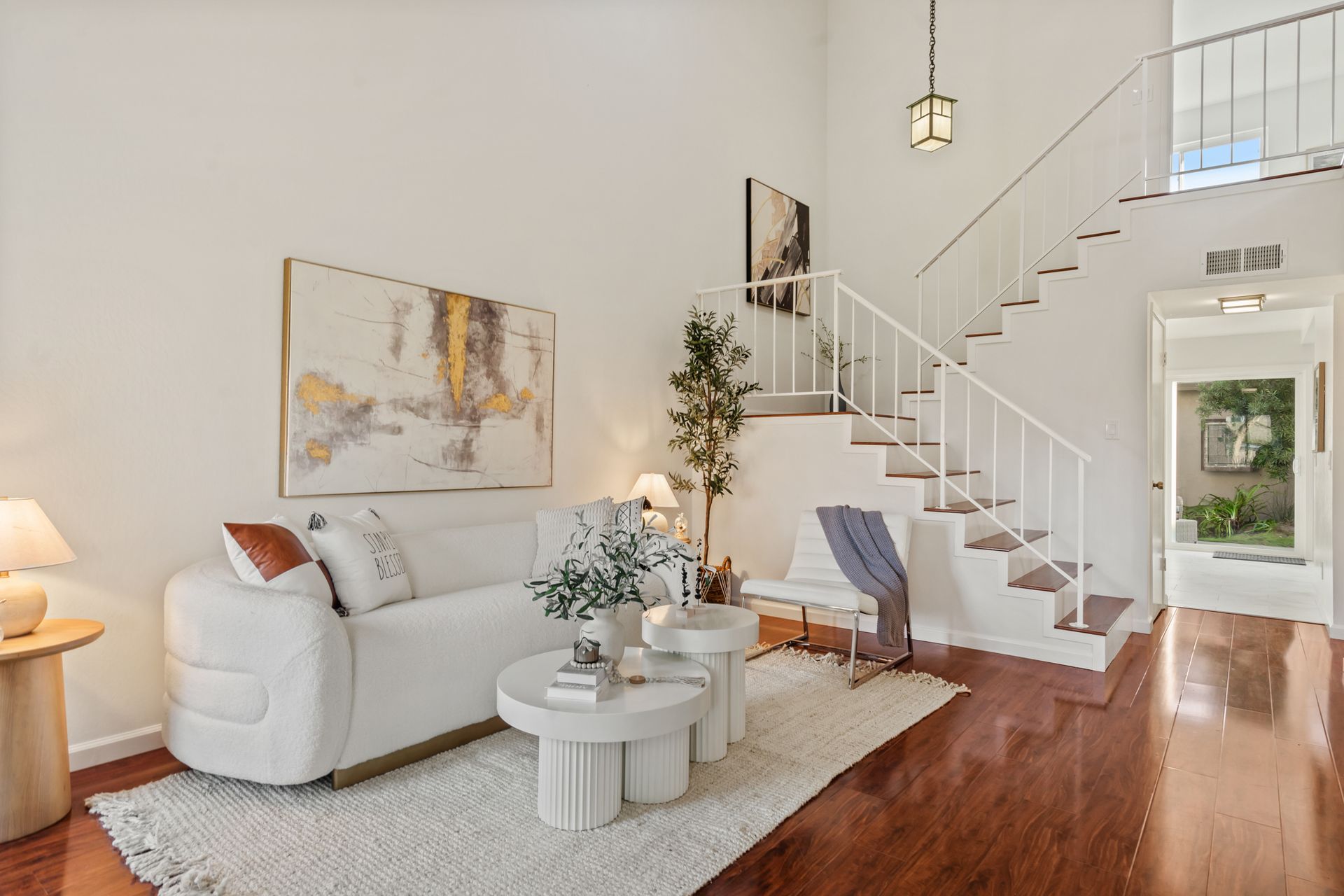 A living room with a white couch , table , chair and stairs.