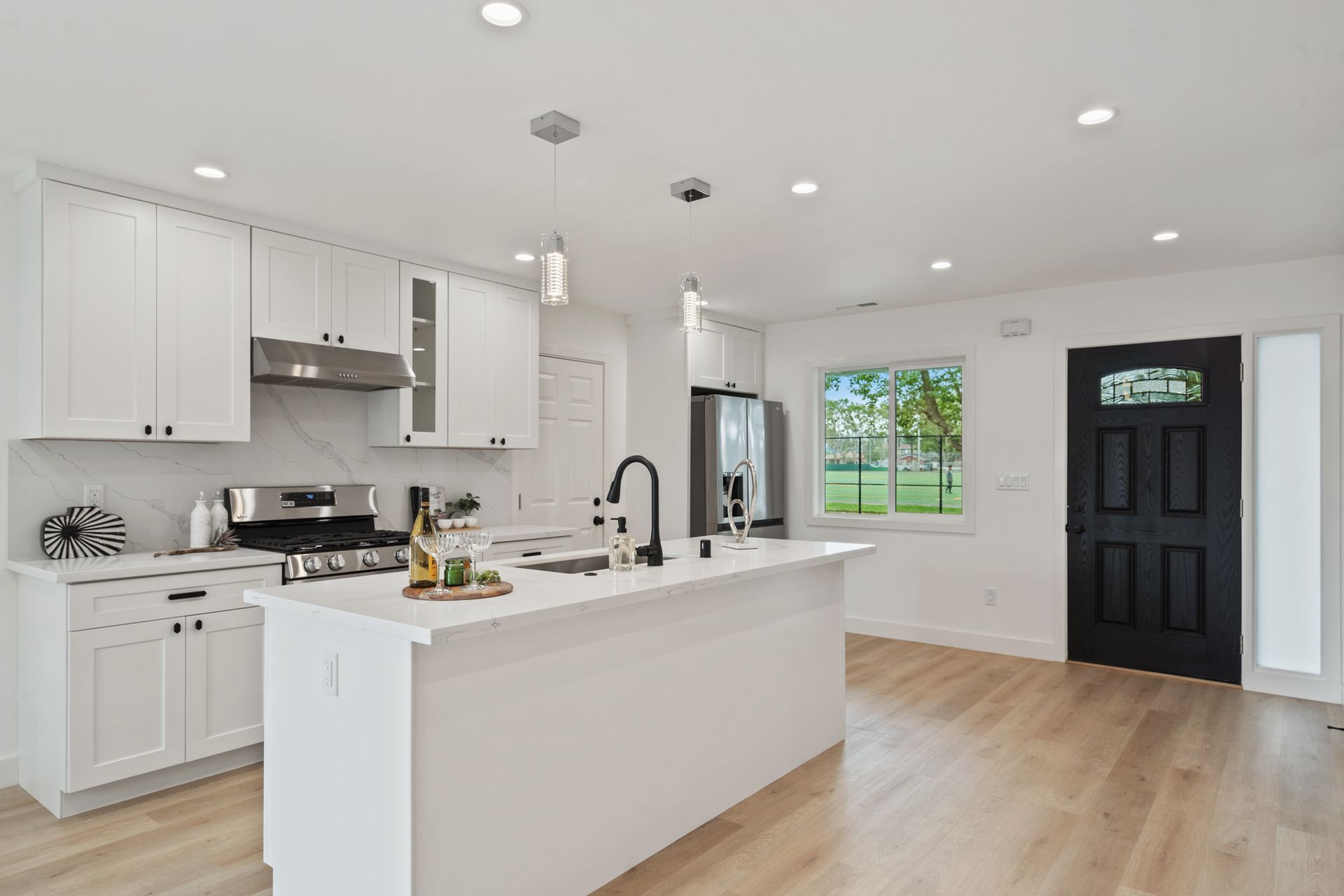 A kitchen with white cabinets , stainless steel appliances , a large island and a black door.
