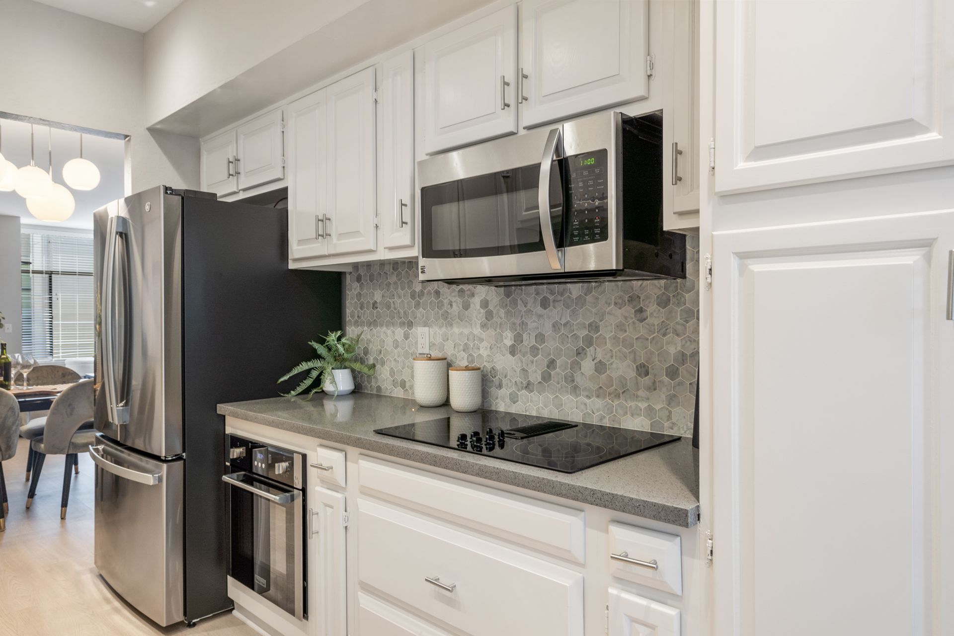 A kitchen with white cabinets , stainless steel appliances , a stove , microwave and refrigerator.