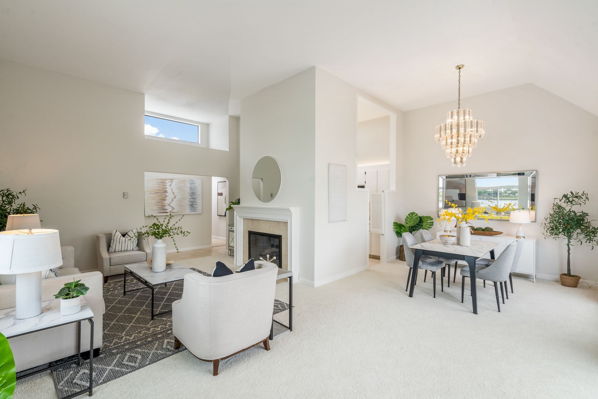 A living room and dining room in a house with white furniture and a fireplace.