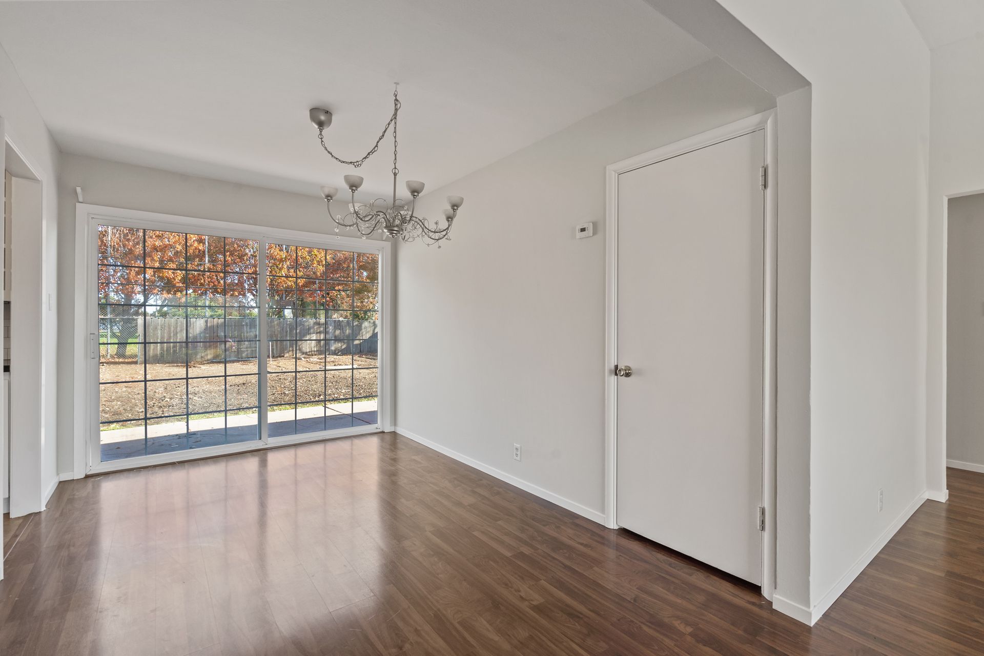 An empty dining room with hardwood floors and sliding glass doors.