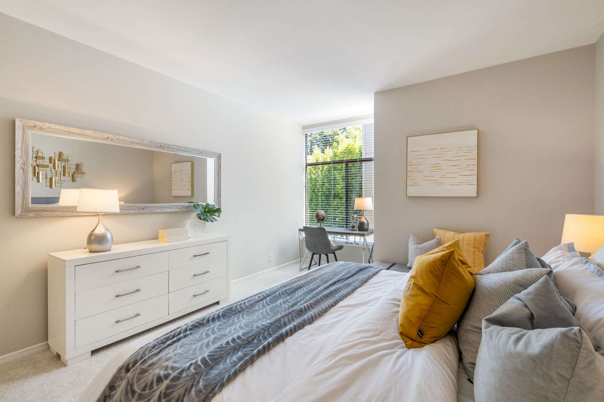 A bedroom with a large bed , dresser , mirror and window.