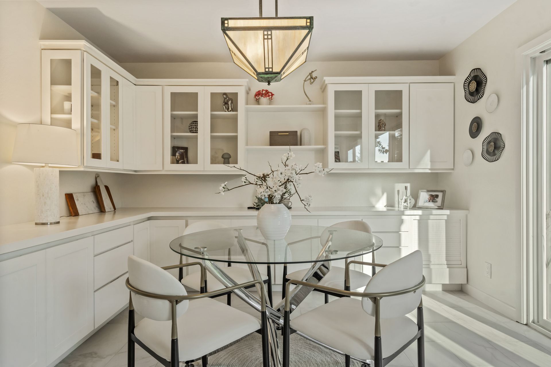 A dining room with a glass table and chairs and white cabinets