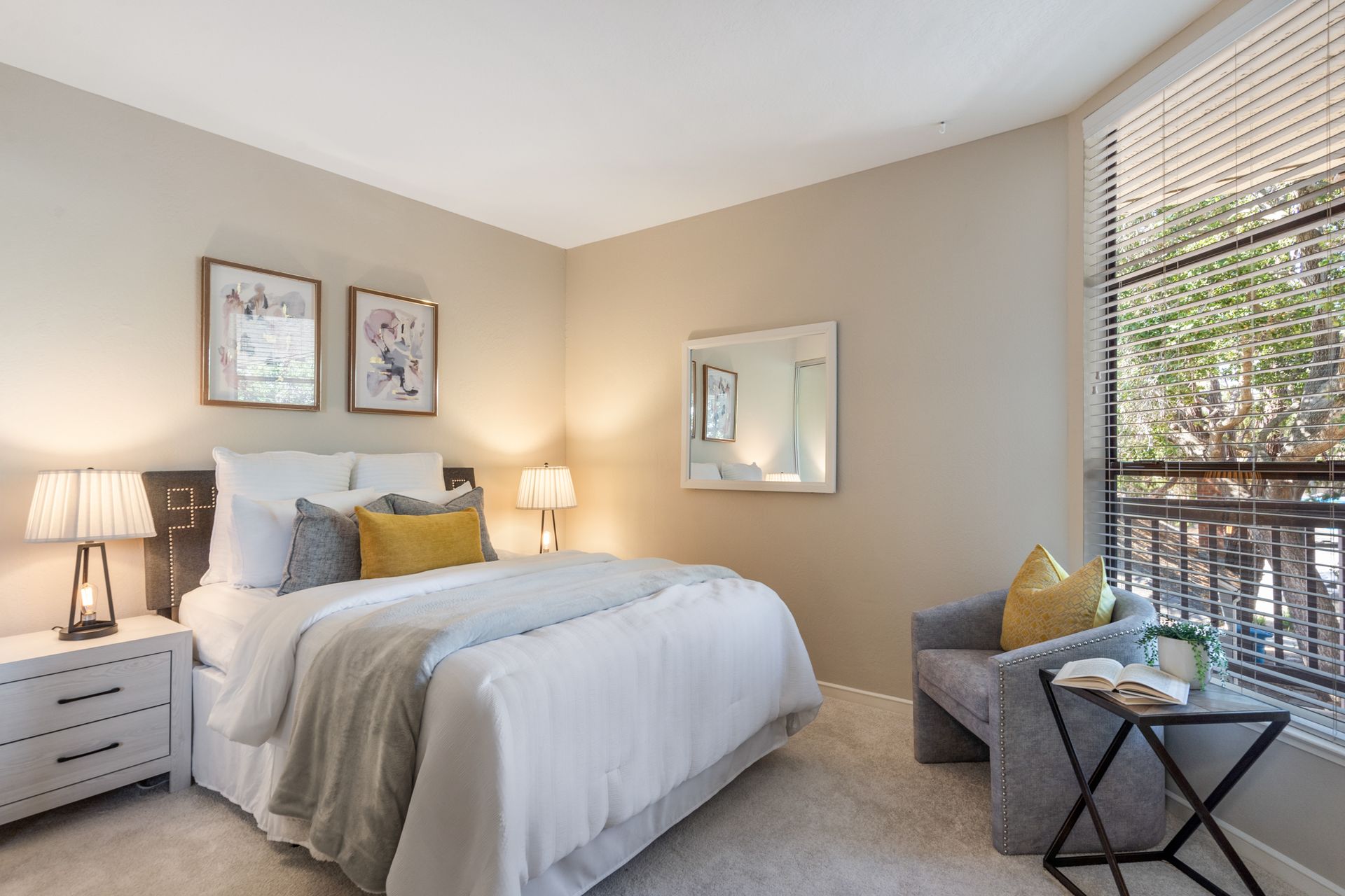 A bedroom with a bed , chair , nightstand , mirror and window.