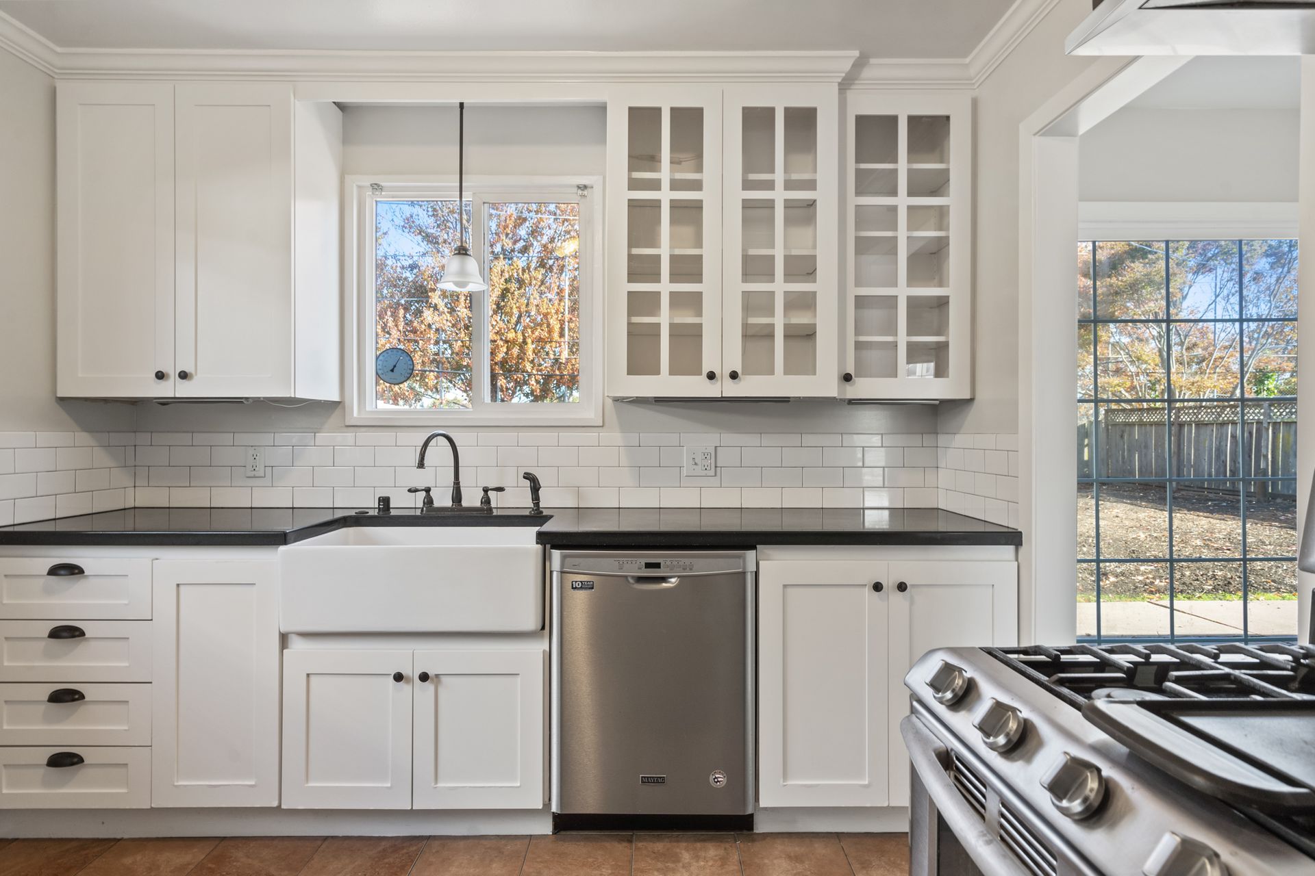 A kitchen with white cabinets , a stove , a sink , and a window.