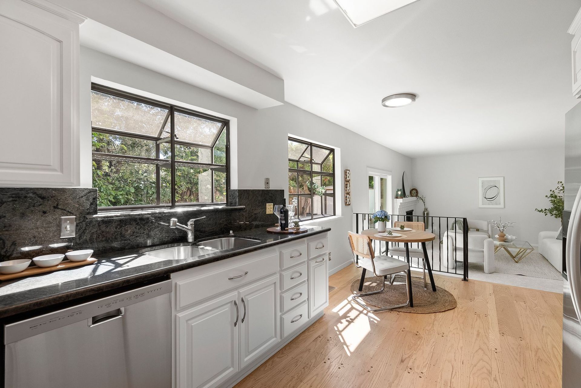 A kitchen with white cabinets , black counter tops , stainless steel appliances and hardwood floors.