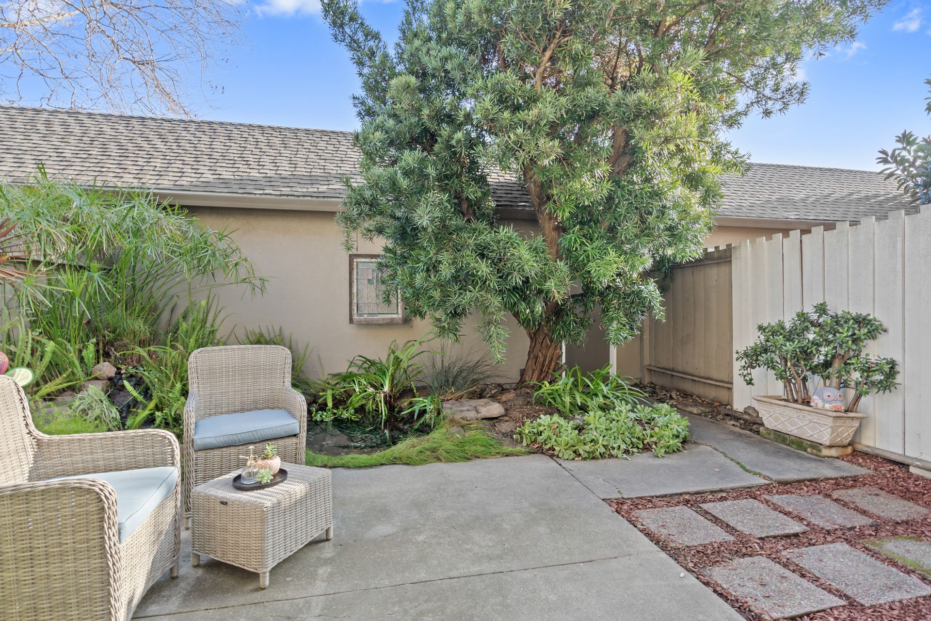 A patio with chairs , a table and a tree in front of a house.