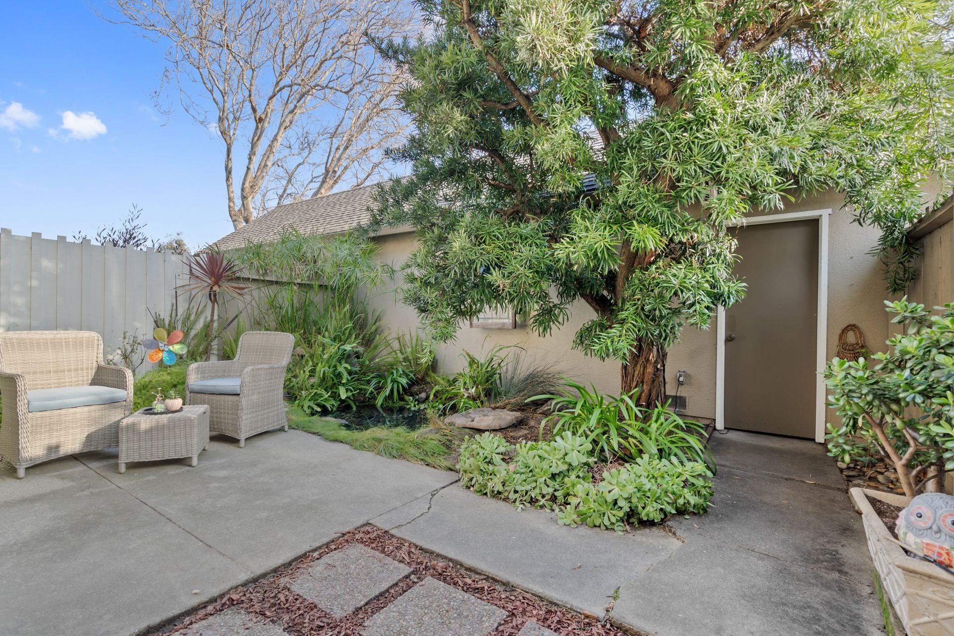 A patio with furniture and a tree in the backyard of a house.