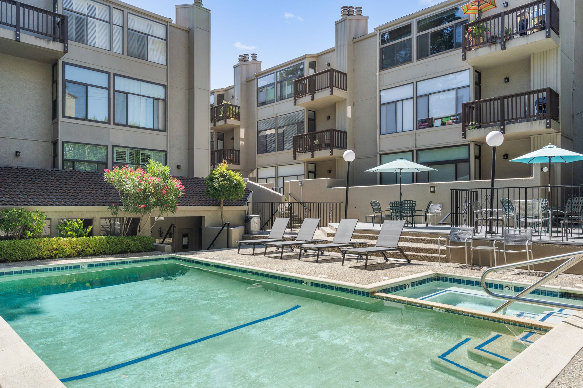 A large swimming pool surrounded by chairs and umbrellas in front of a building.
