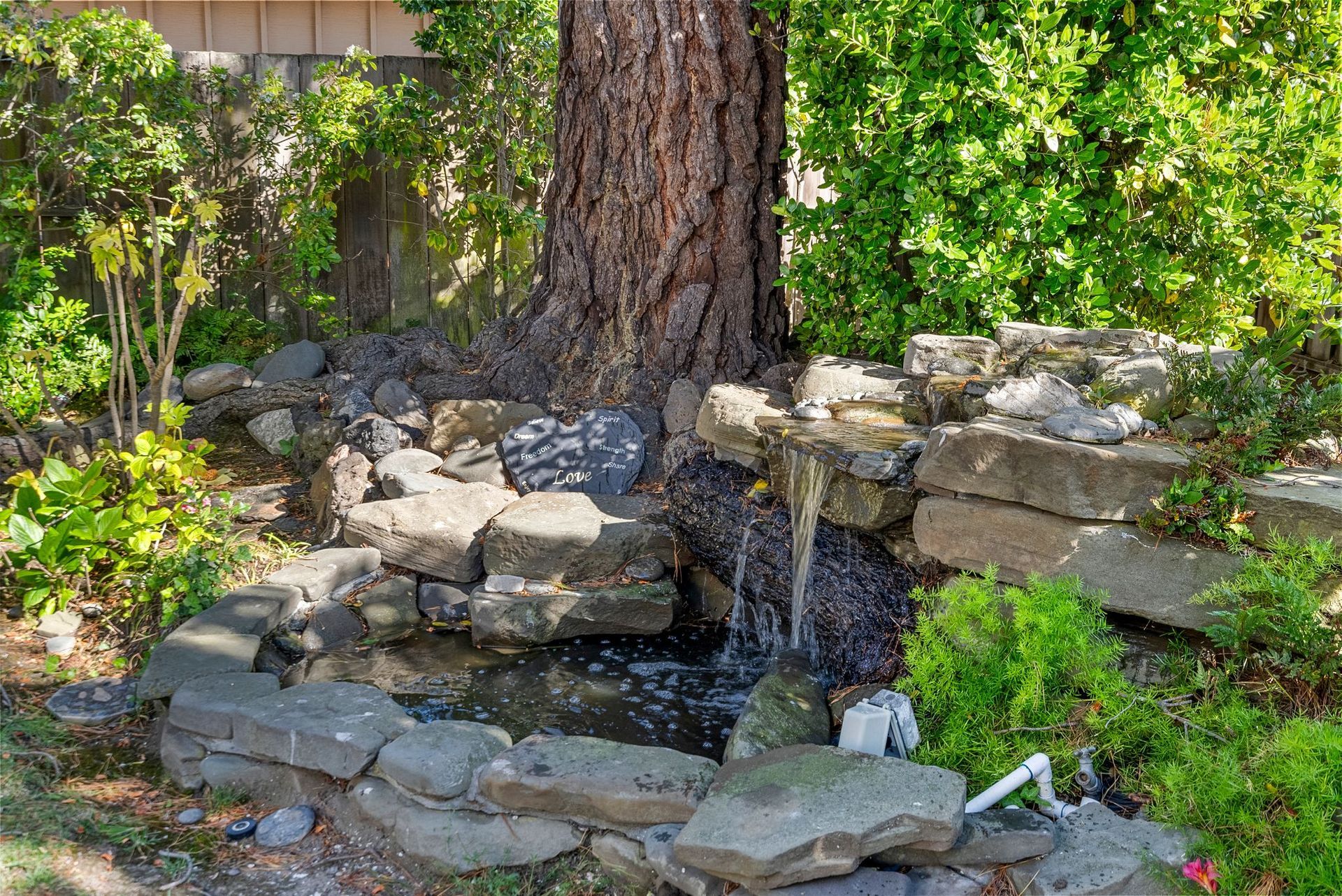 A small waterfall is surrounded by rocks and trees in a garden.