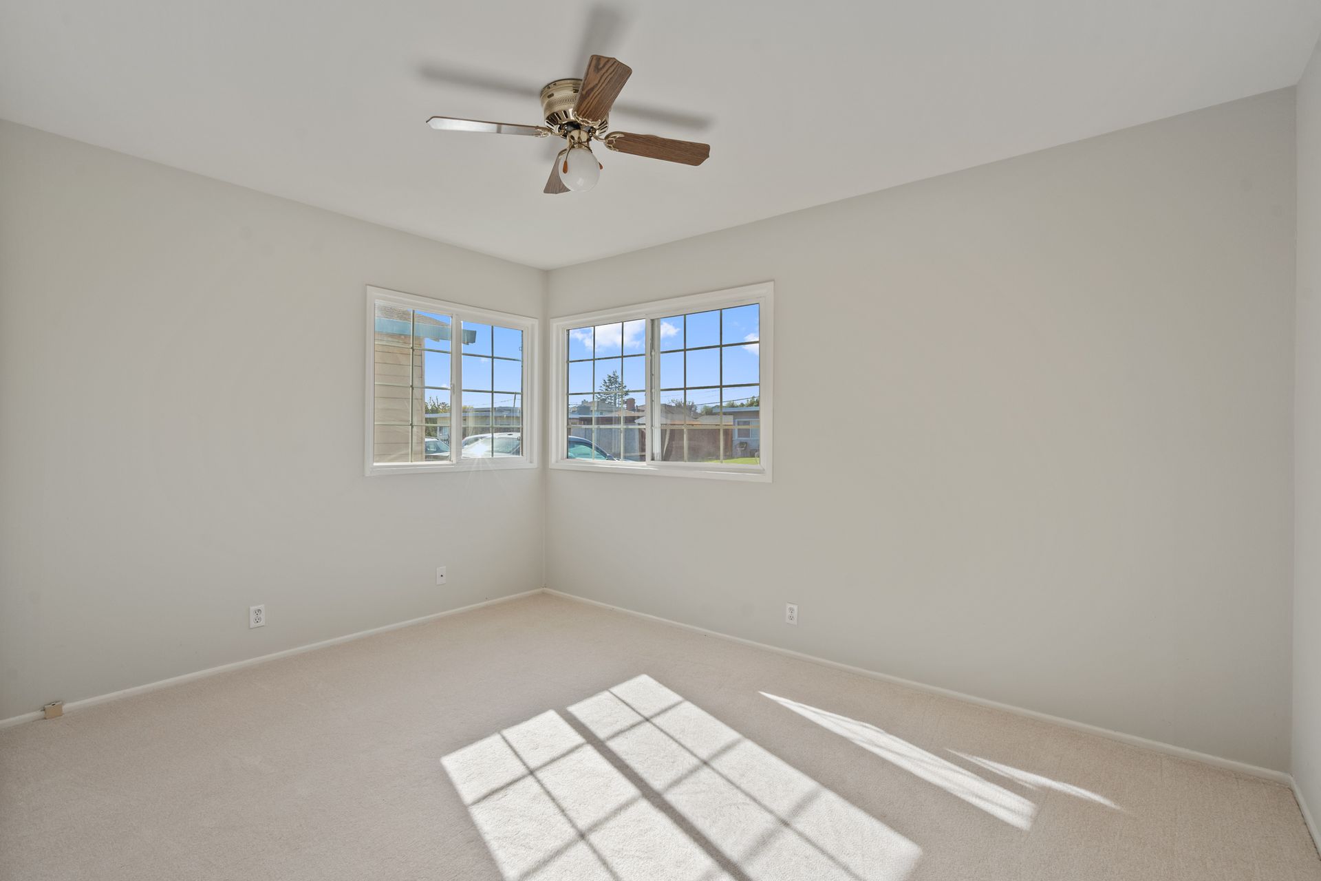 An empty bedroom with a ceiling fan and two windows.