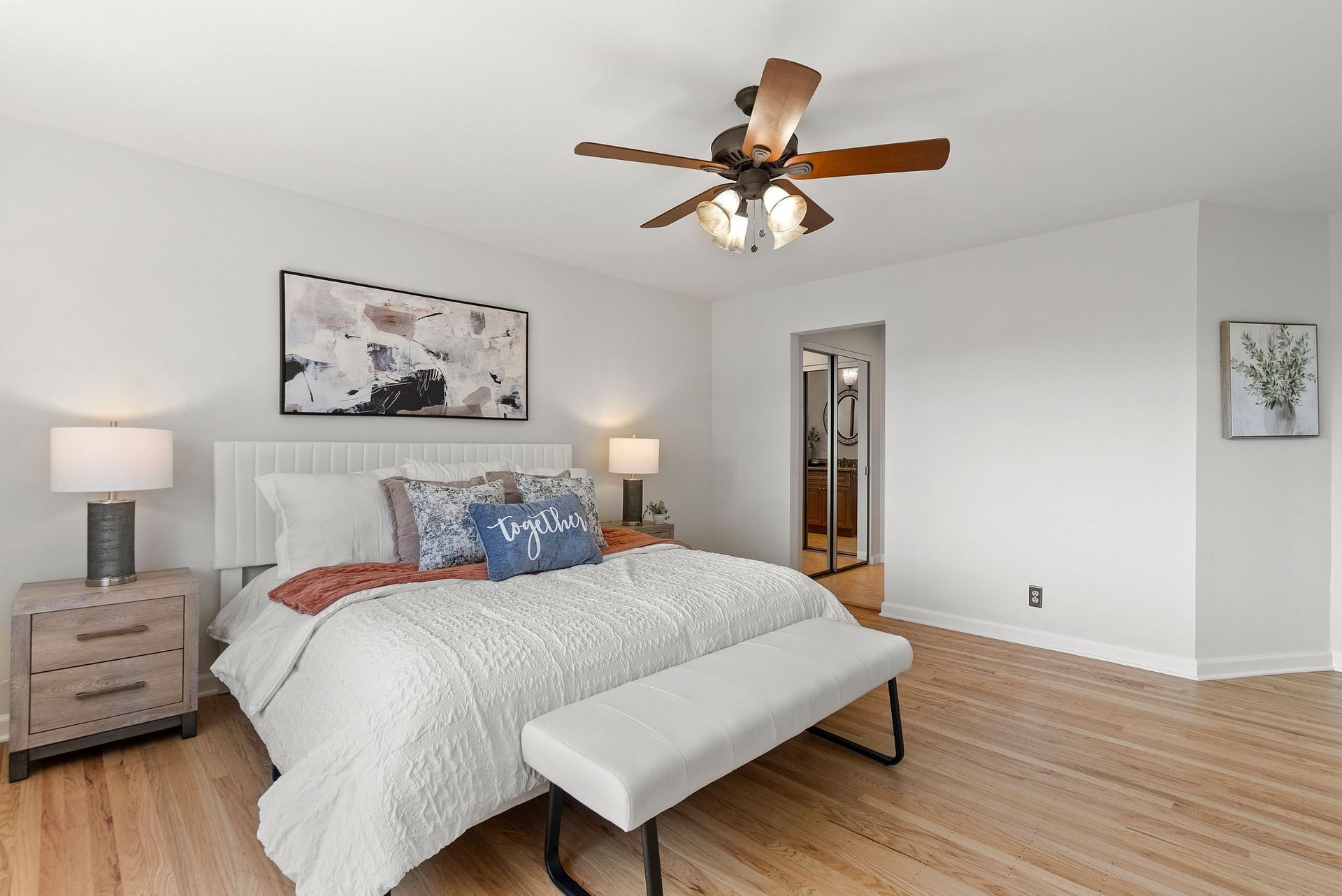 A bedroom with a bed , nightstand , bench and ceiling fan.