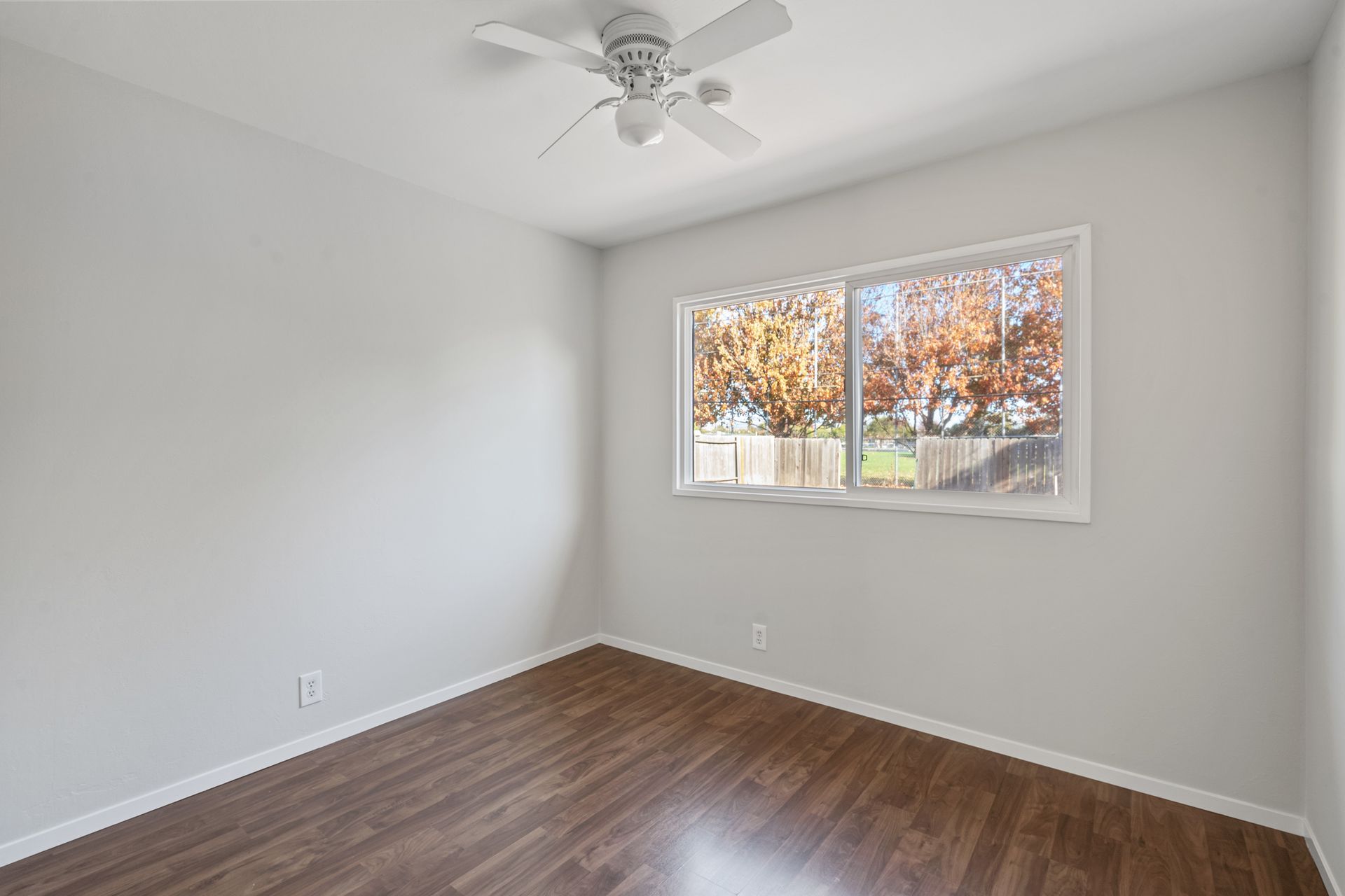 An empty bedroom with hardwood floors and a ceiling fan.