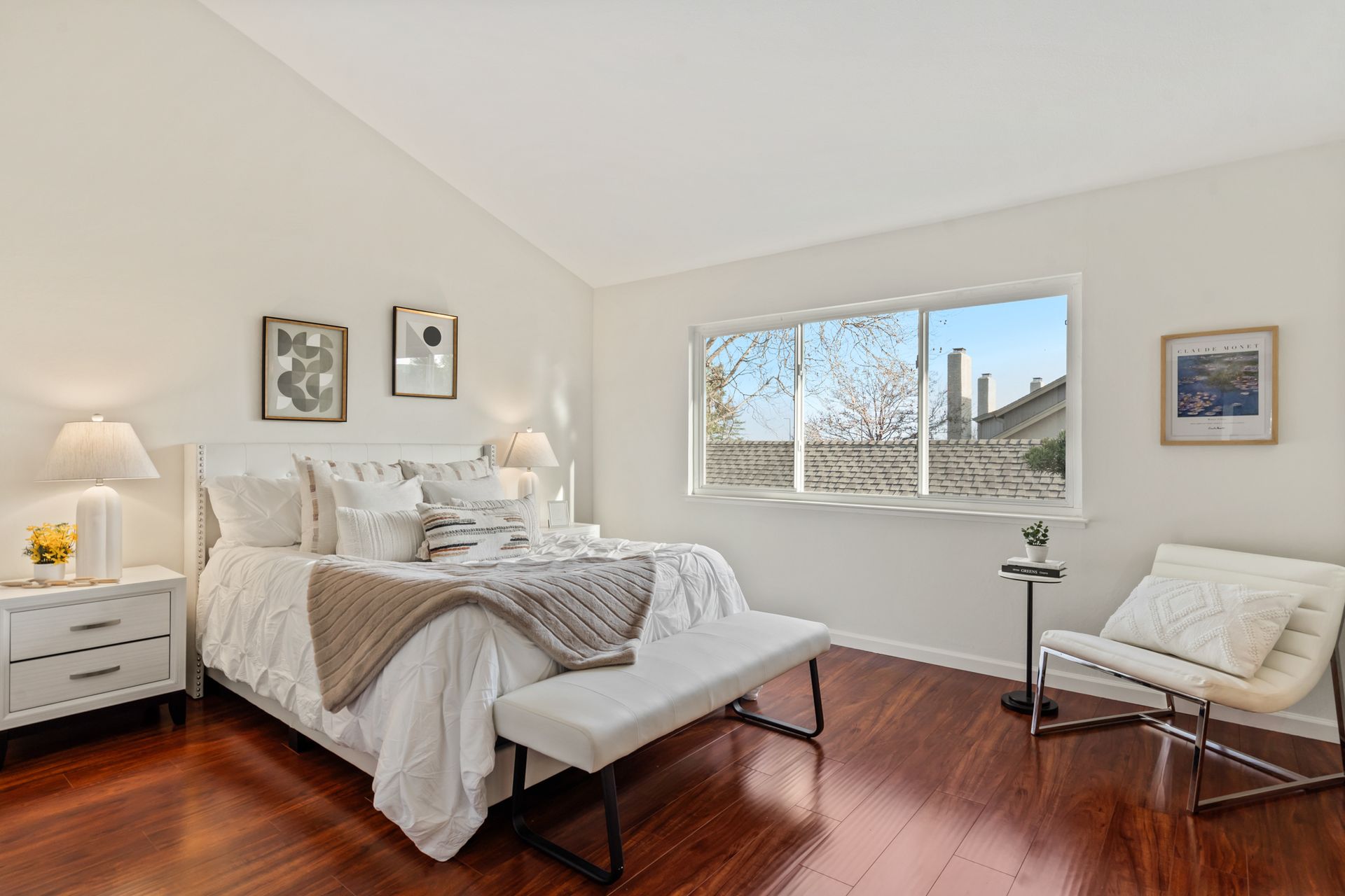 A bedroom with a bed , chair , bench and window.