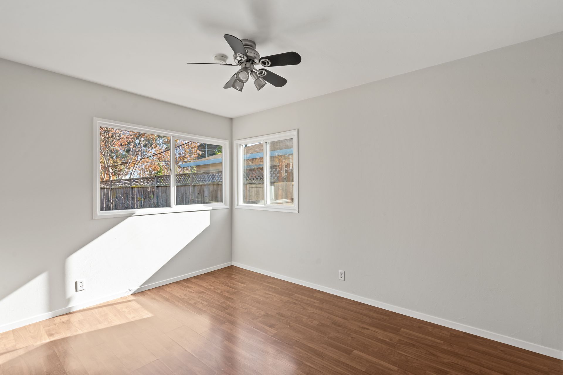 An empty room with a ceiling fan and two windows.