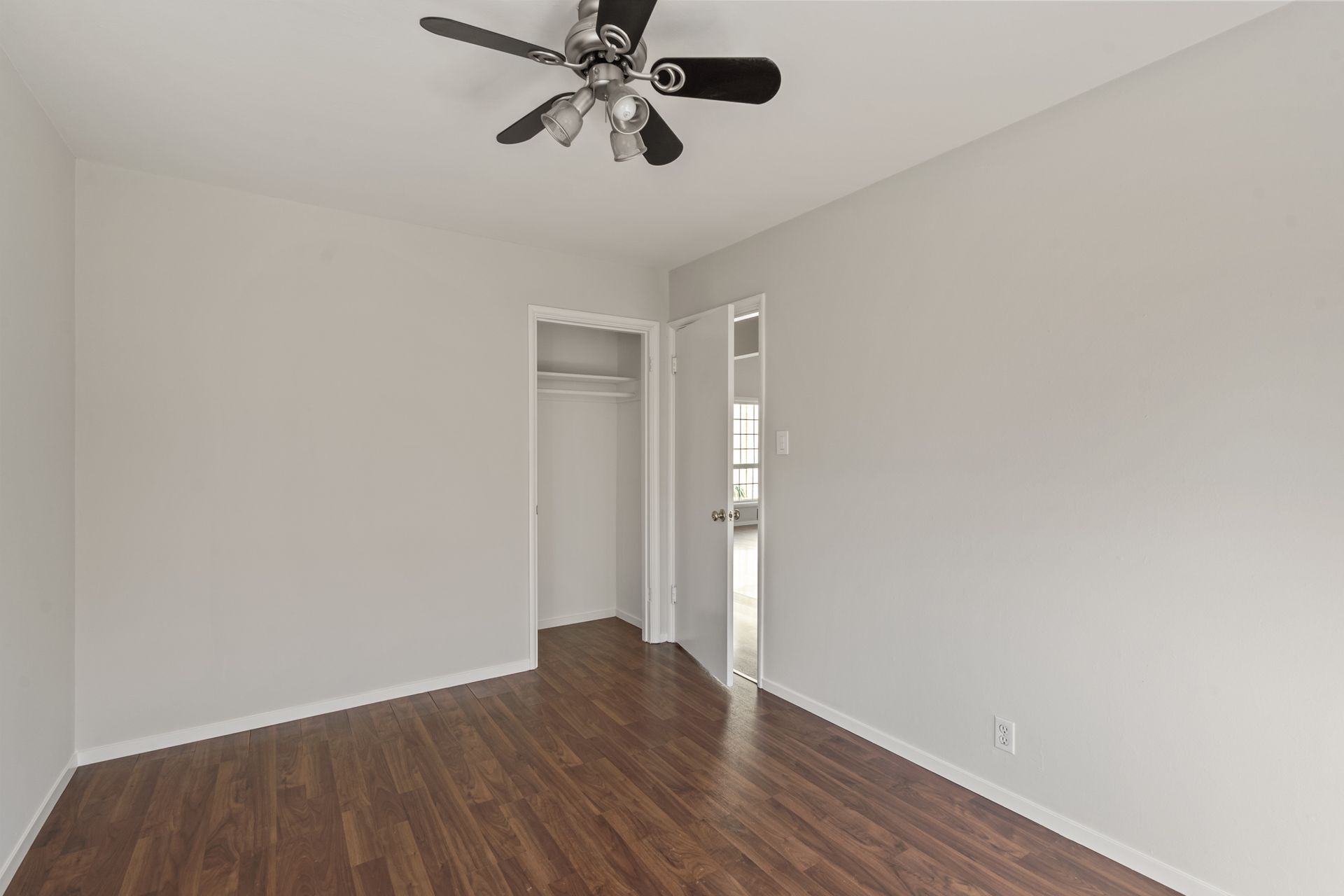 An empty bedroom with hardwood floors and a ceiling fan.