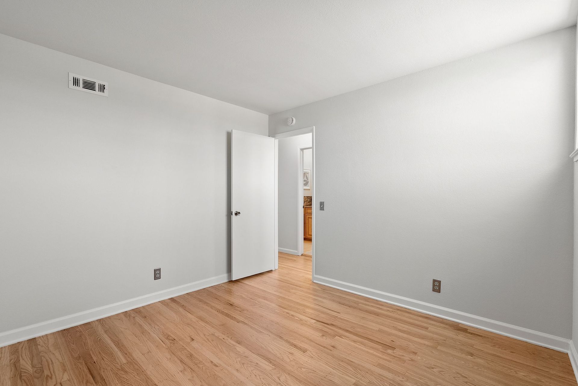 An empty bedroom with hardwood floors and white walls.