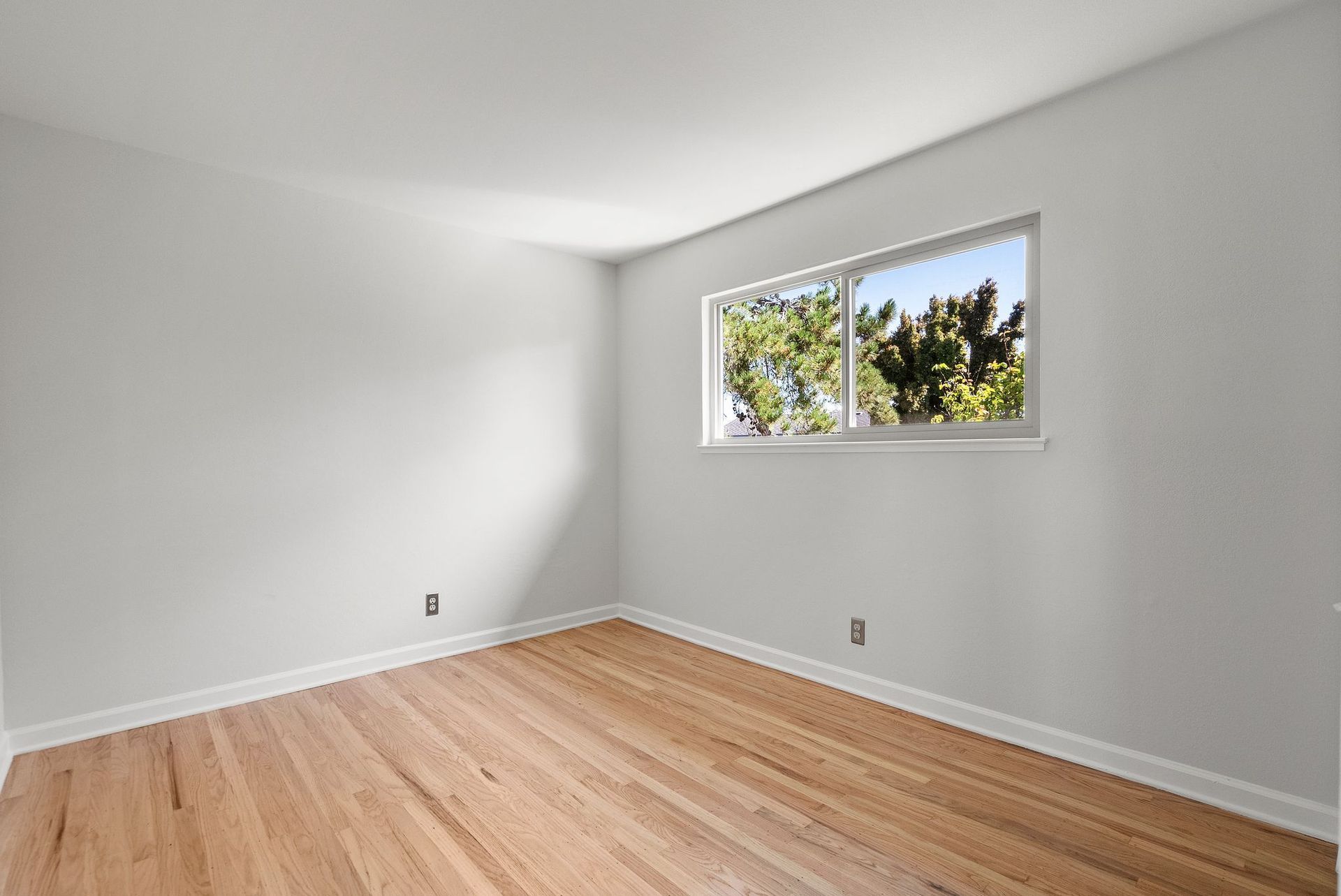 An empty room with hardwood floors and a window.