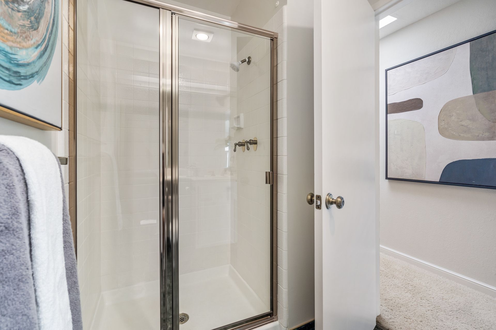 A bathroom with a walk in shower and a painting on the wall.