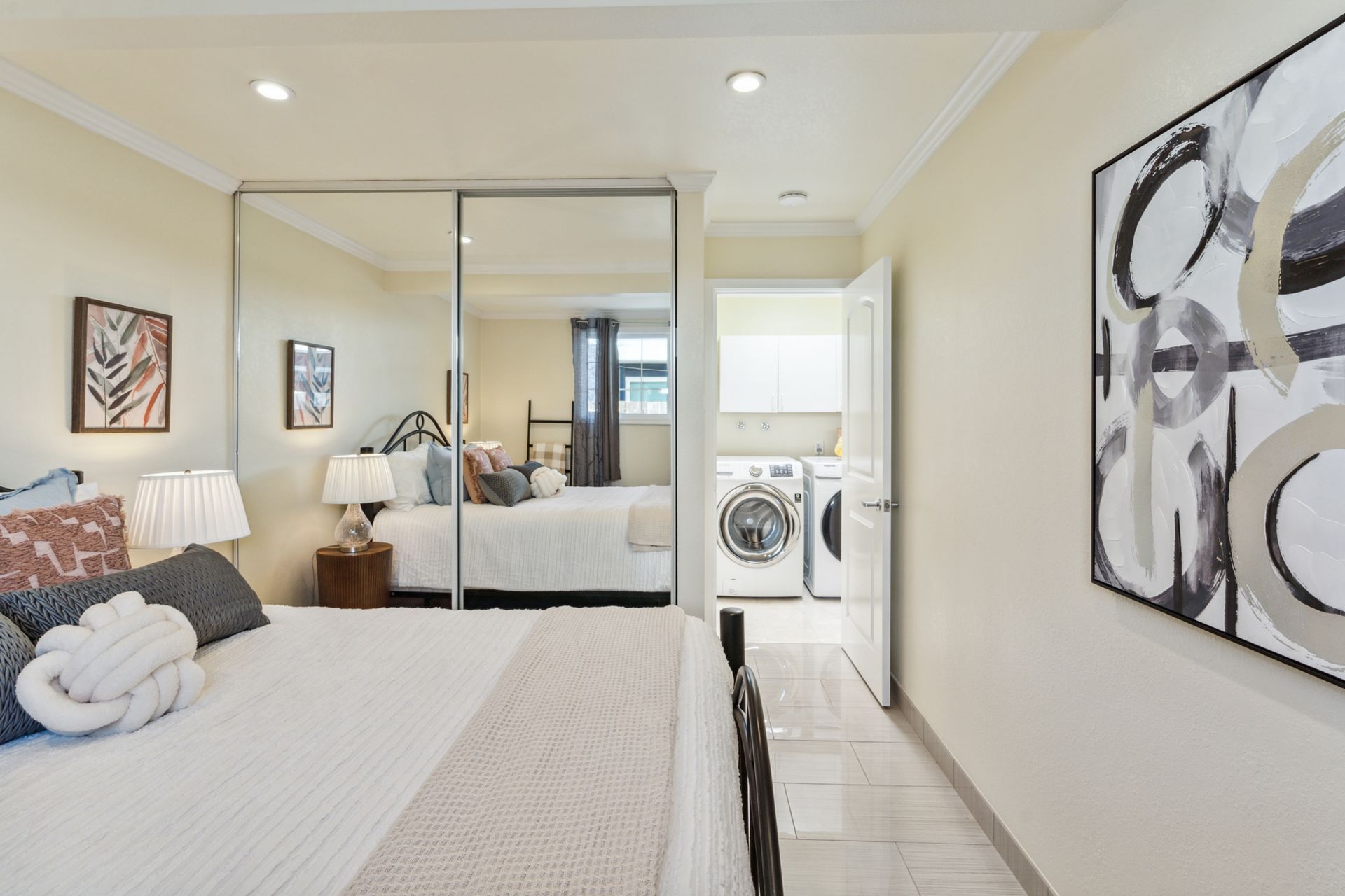 A bedroom with a bed , sliding glass doors , a washer and dryer and a painting on the wall.
