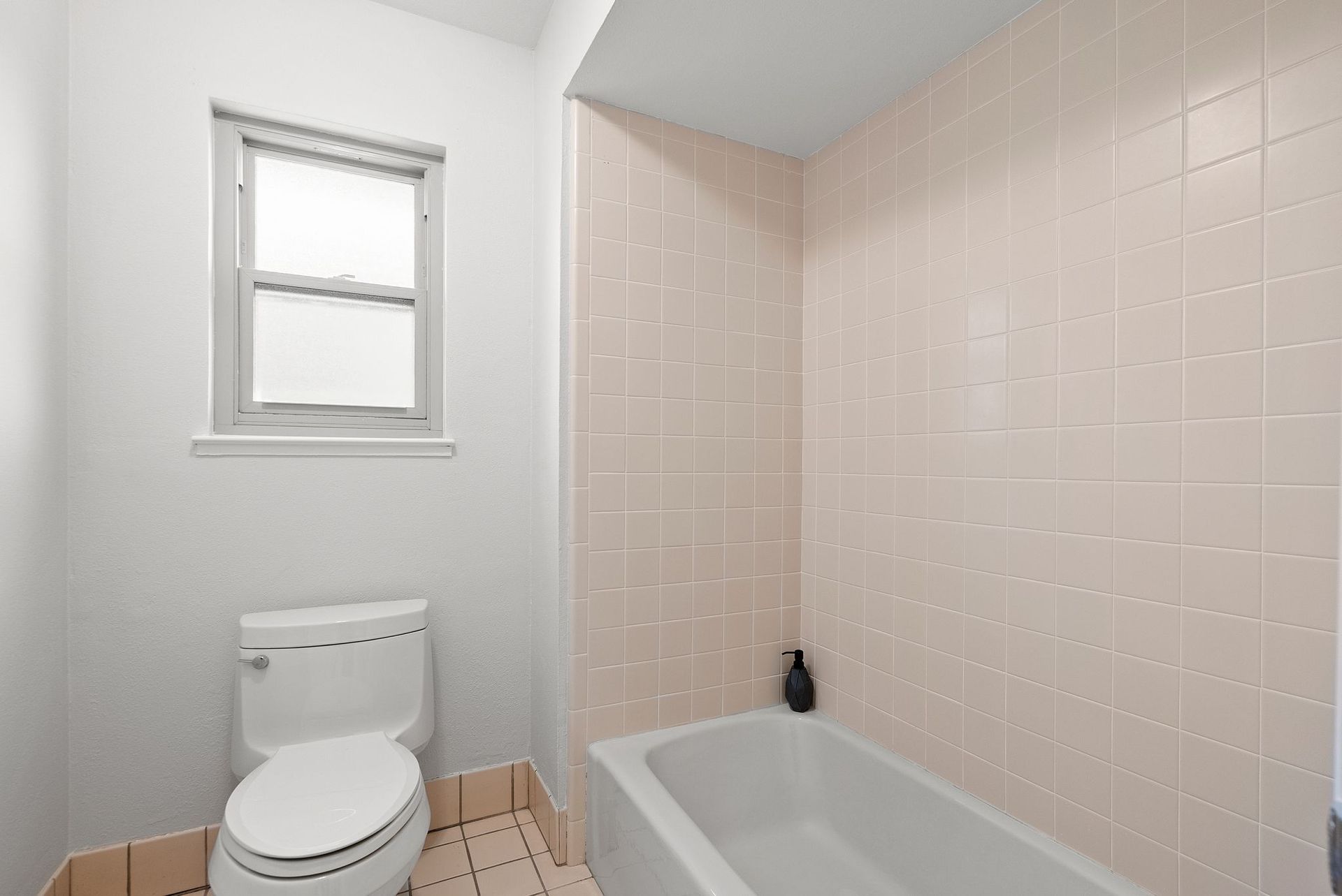 A bathroom with a toilet , bathtub and window.