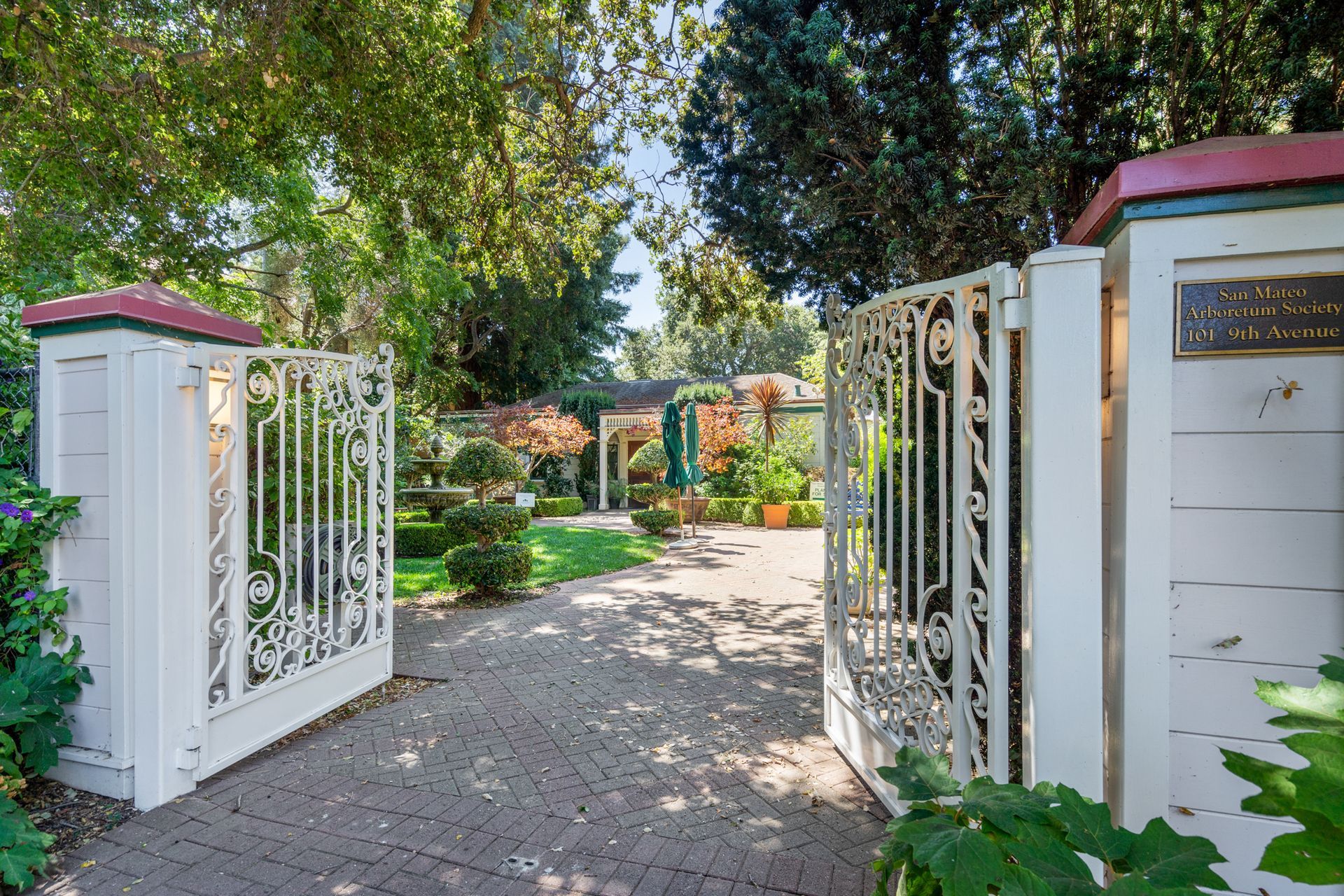 A white gate is open to a driveway leading to a house.