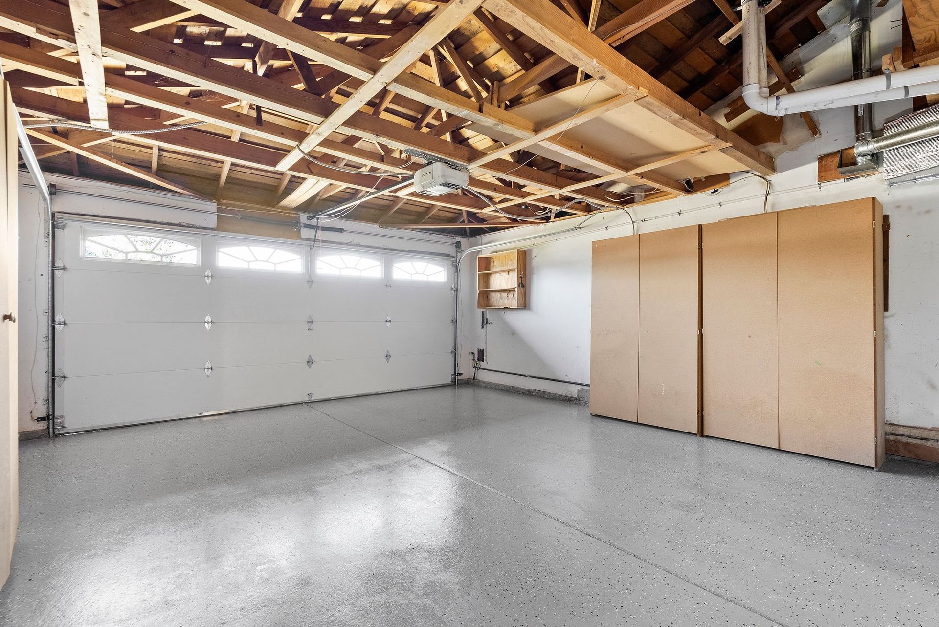 An empty garage with a white garage door and a wooden ceiling.