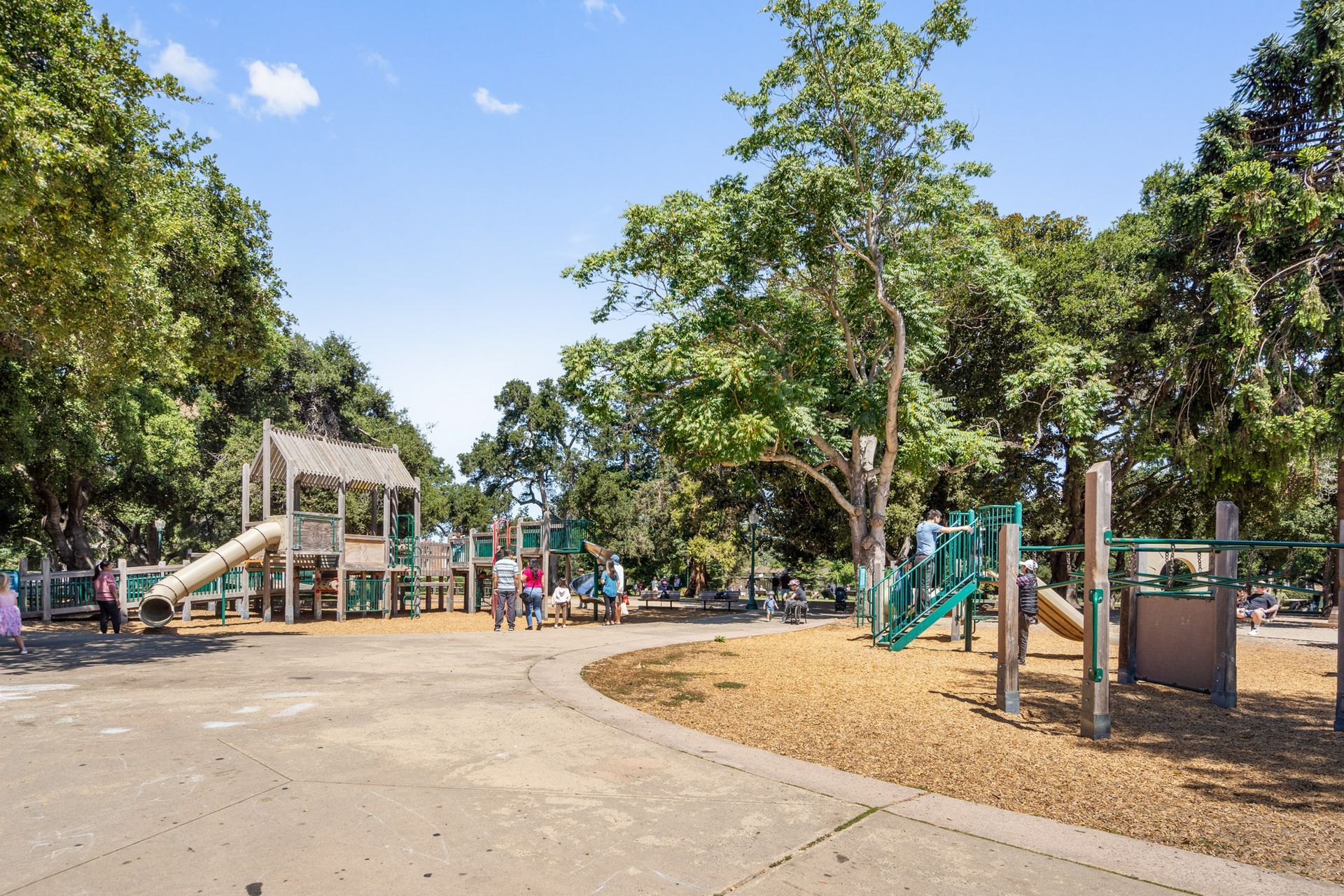 A playground in a park surrounded by trees on a sunny day.