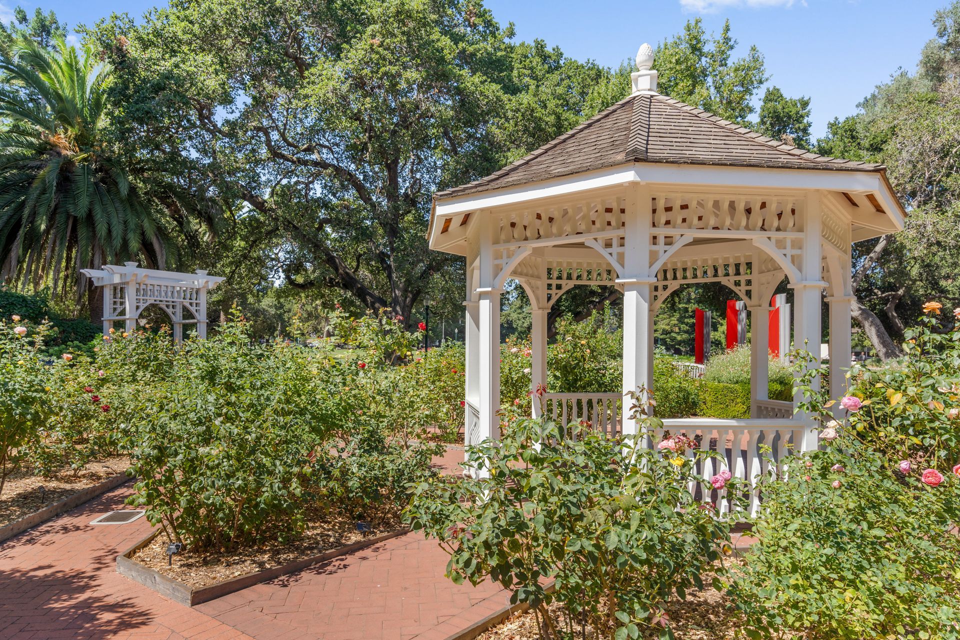 There is a gazebo in the middle of a garden surrounded by trees.
